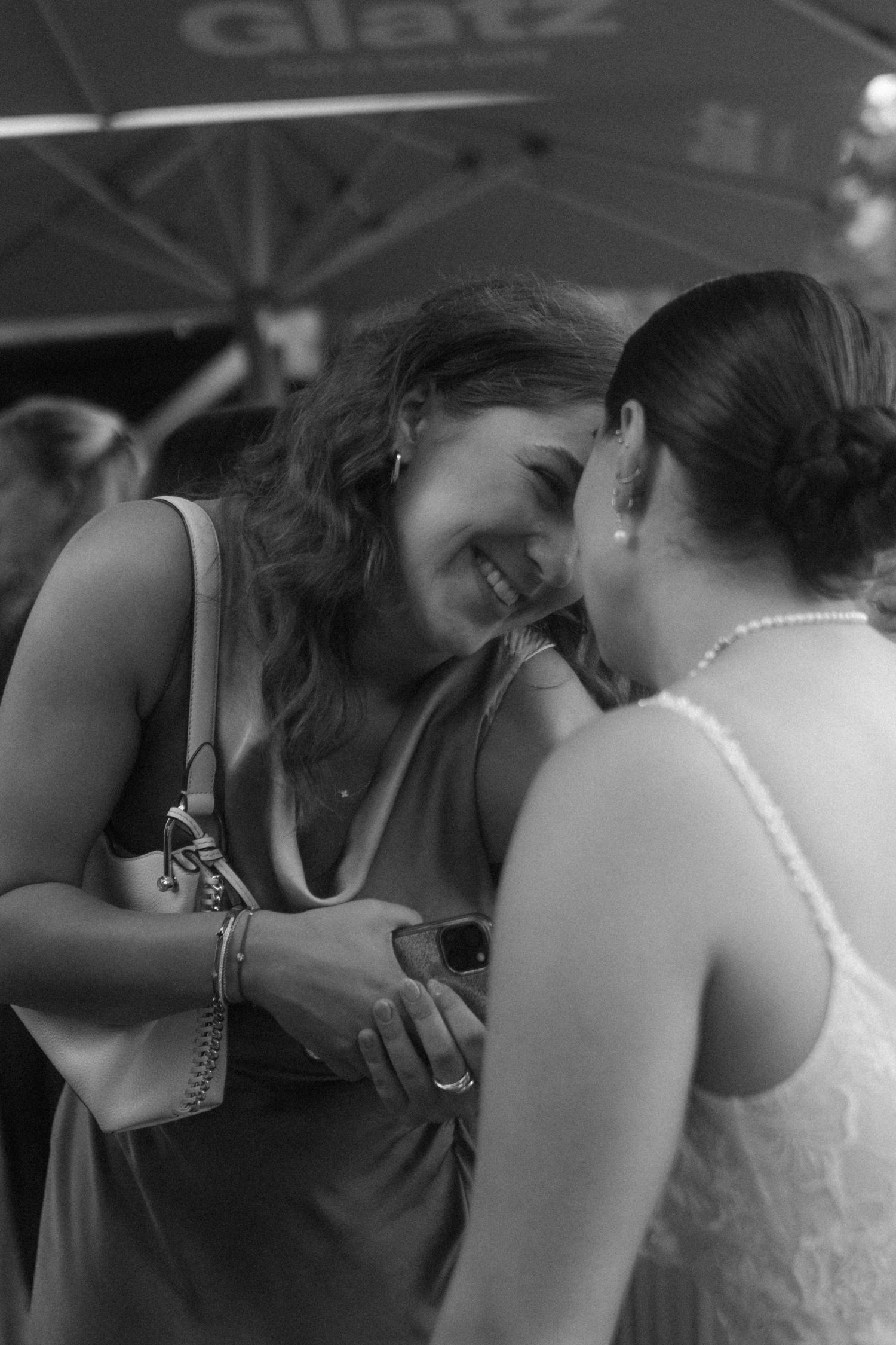 Two guests share a candid laughing moment at a wedding reception captured in black and white.