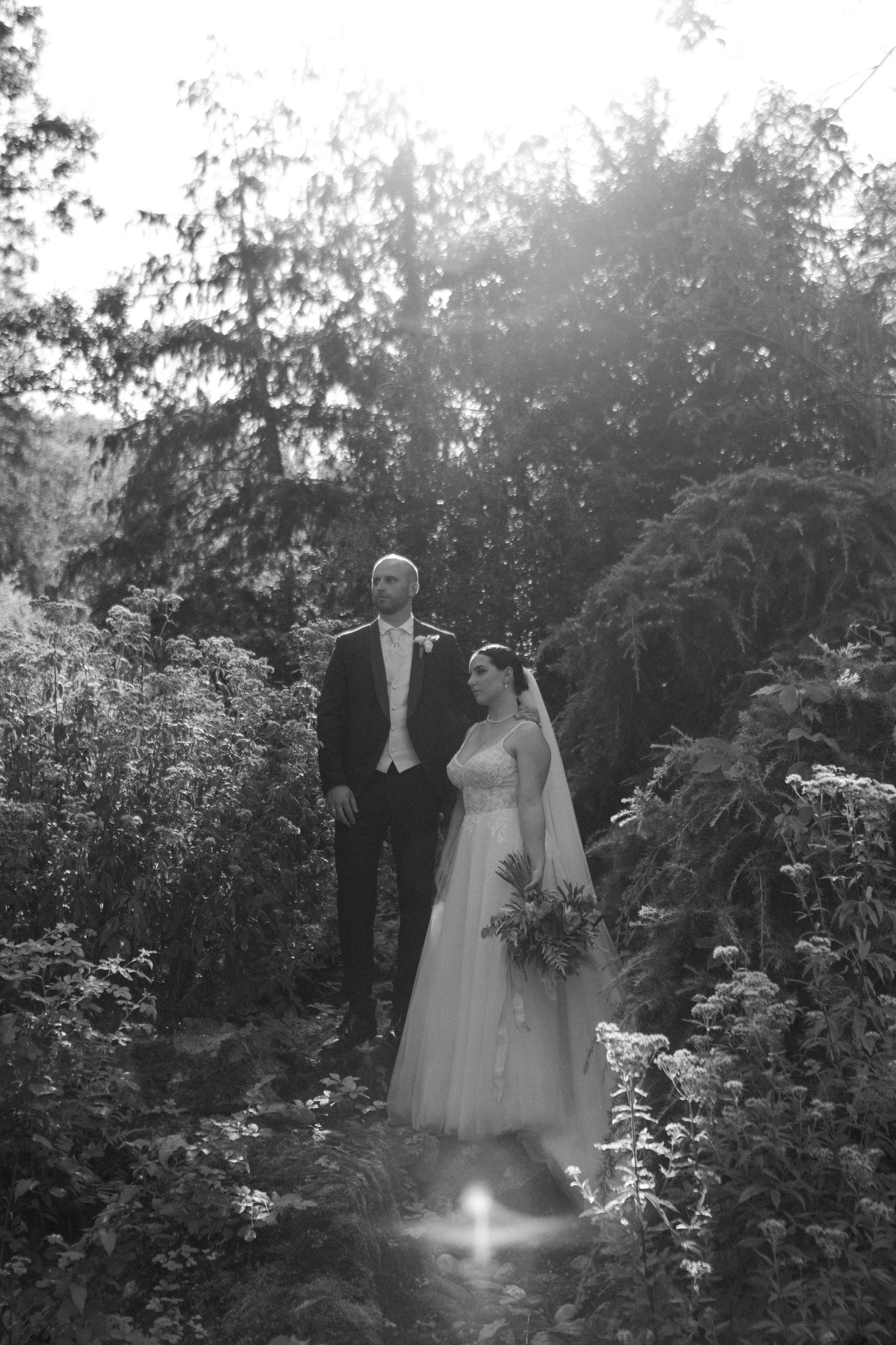 Ethereal wedding portrait of a couple standing among garden foliage with dreamy light.
