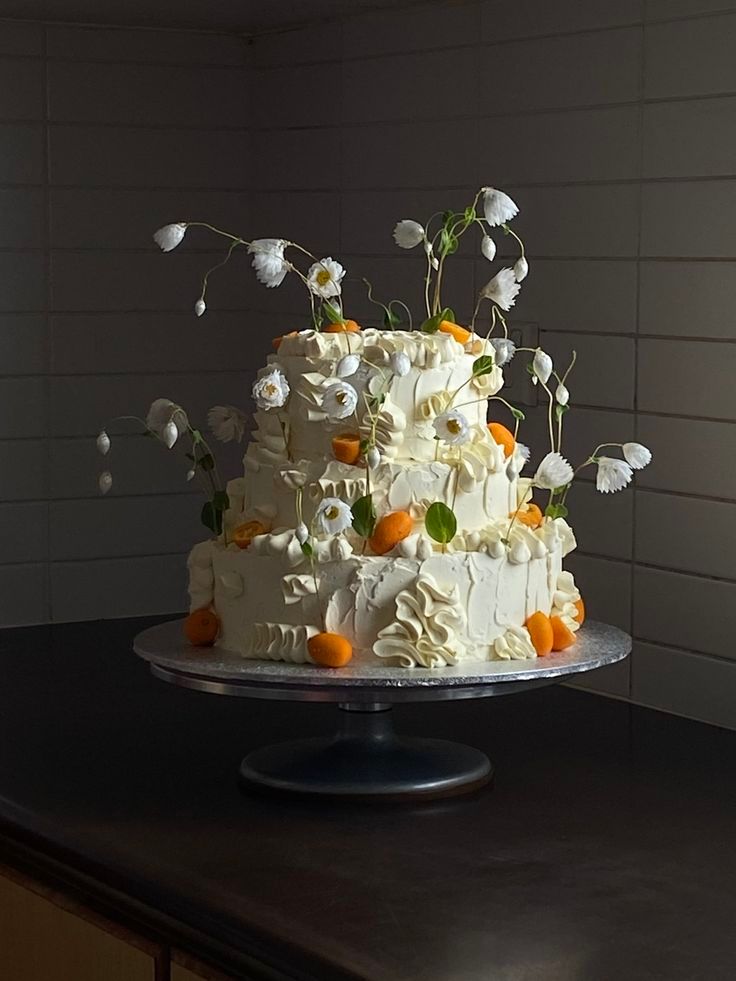 Three-tiered white wedding cake with delicate white flowers and orange accents on dark background.