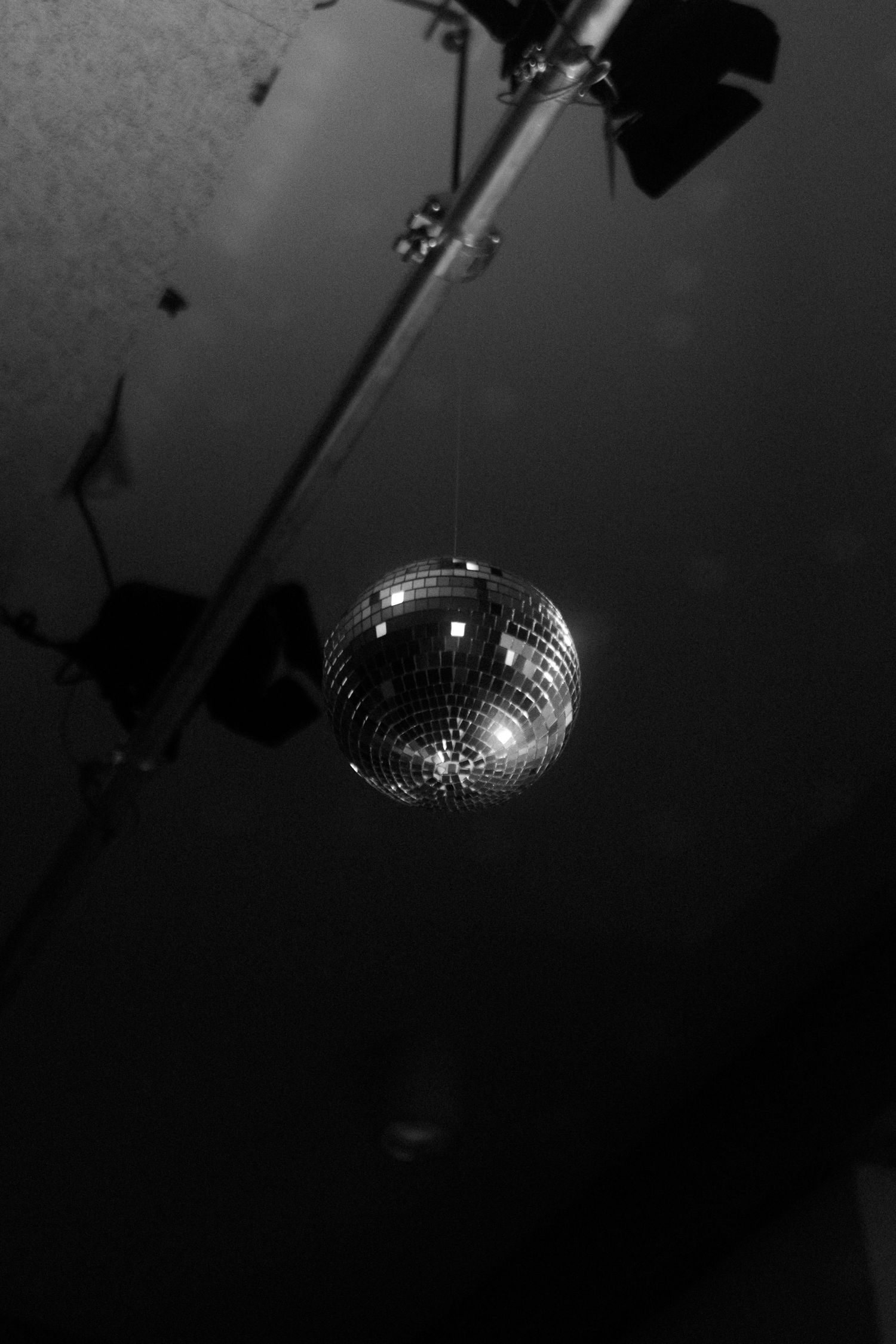 Dramatic black and white photo of a disco ball hanging from ceiling with spotlight.