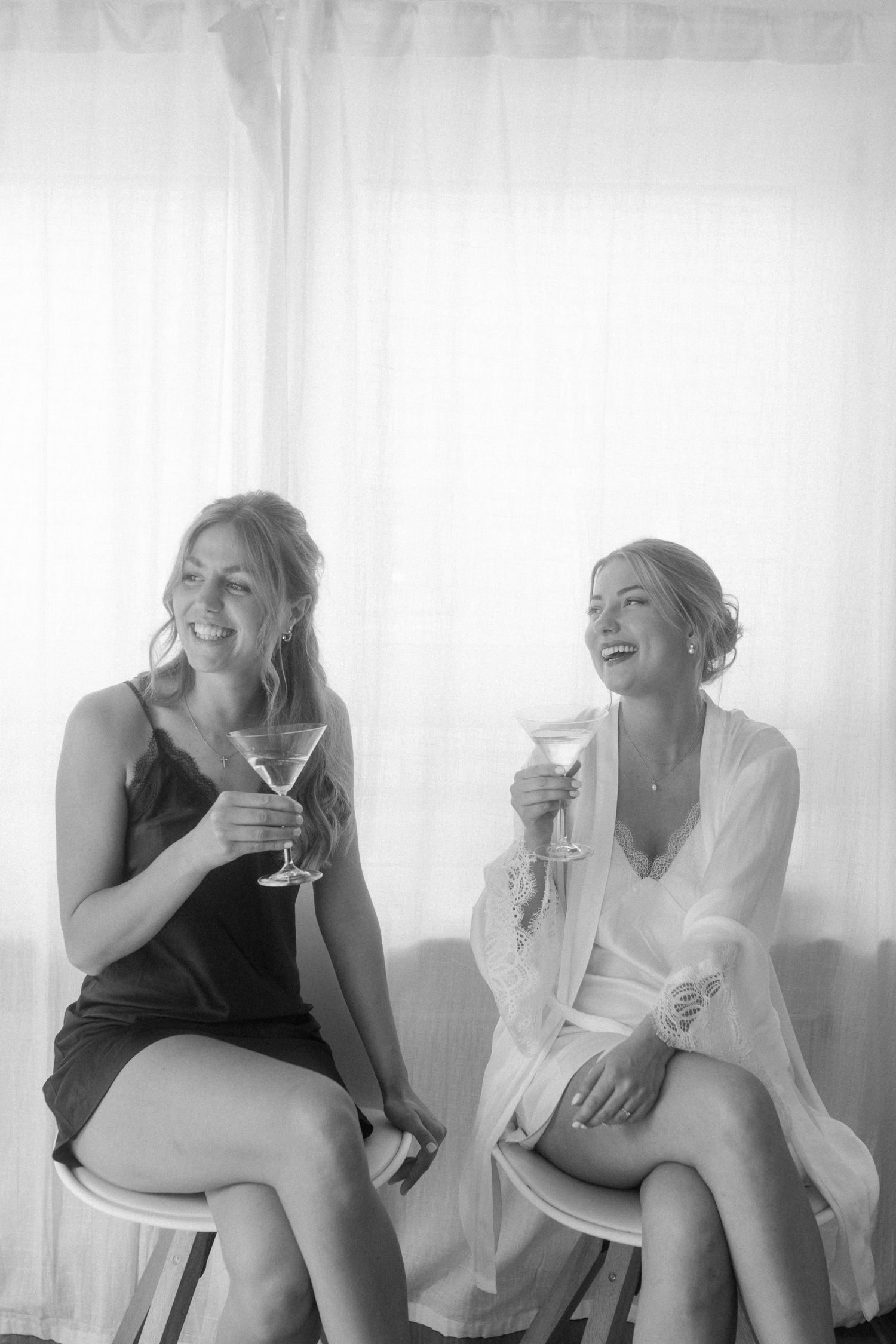Black and white photo of two people enjoying cocktails and laughing together.