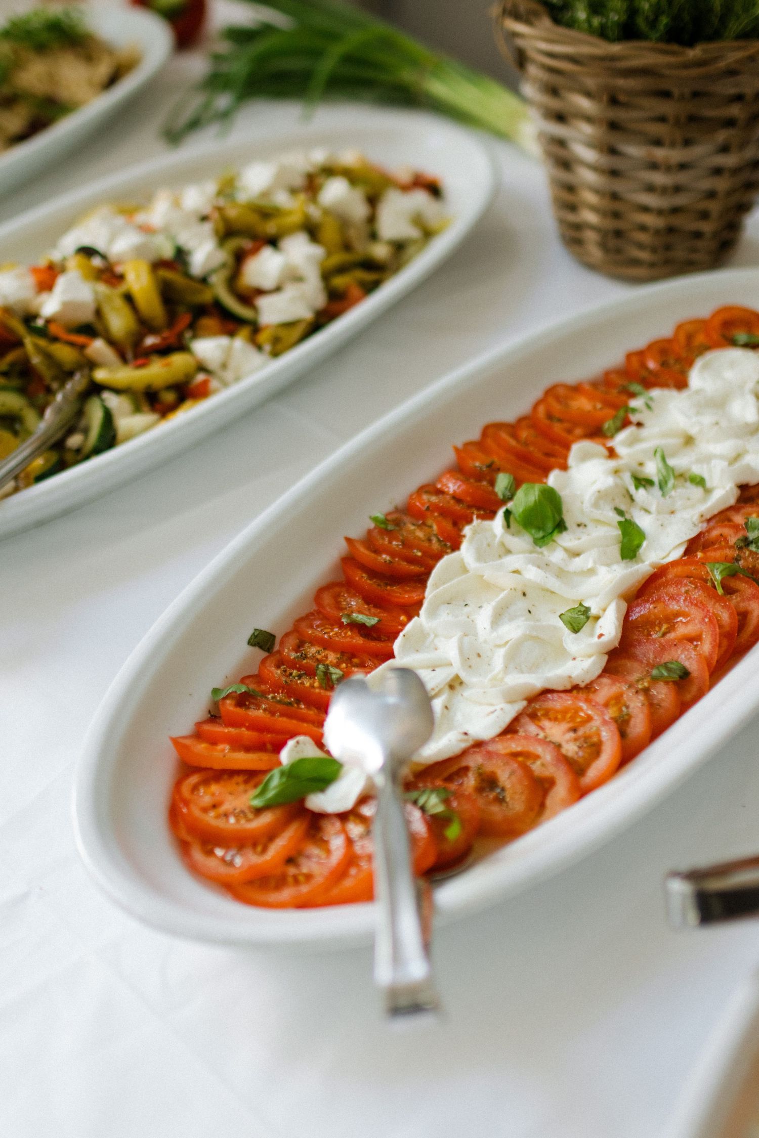 Fresh caprese salad with sliced tomatoes and white sauce arranged on oval serving platter.