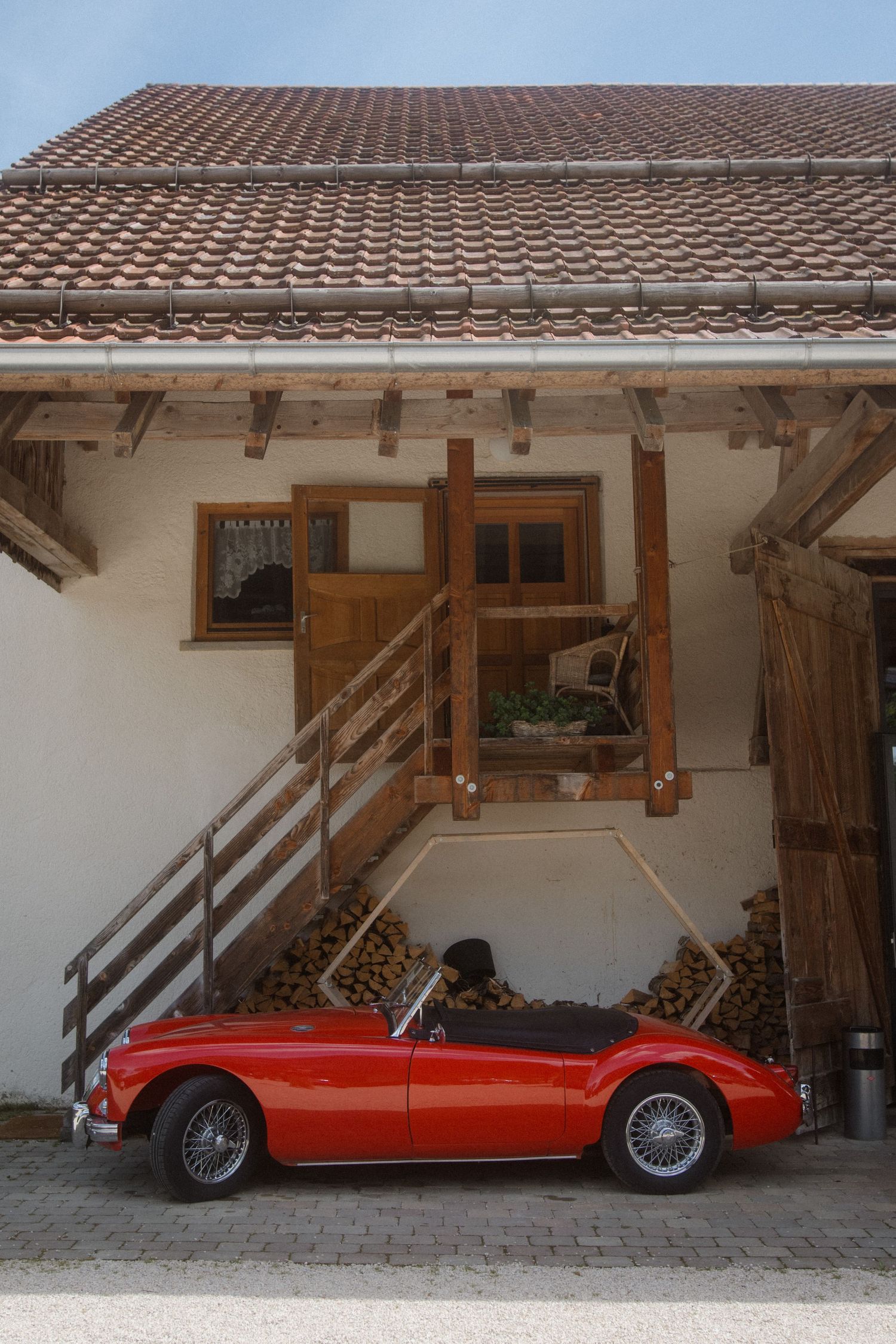 Classic red vintage convertible car parked under traditional white building with wooden accents.