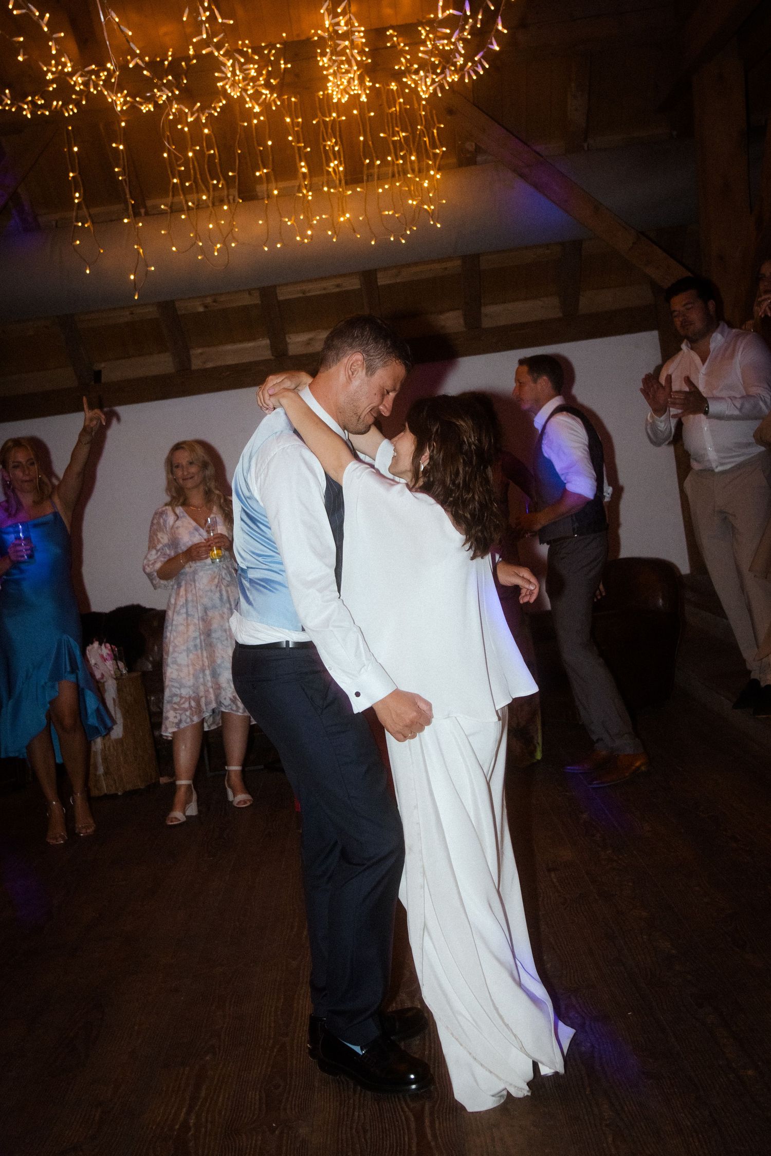 Romantic dance moment under glowing string lights at an indoor reception venue.