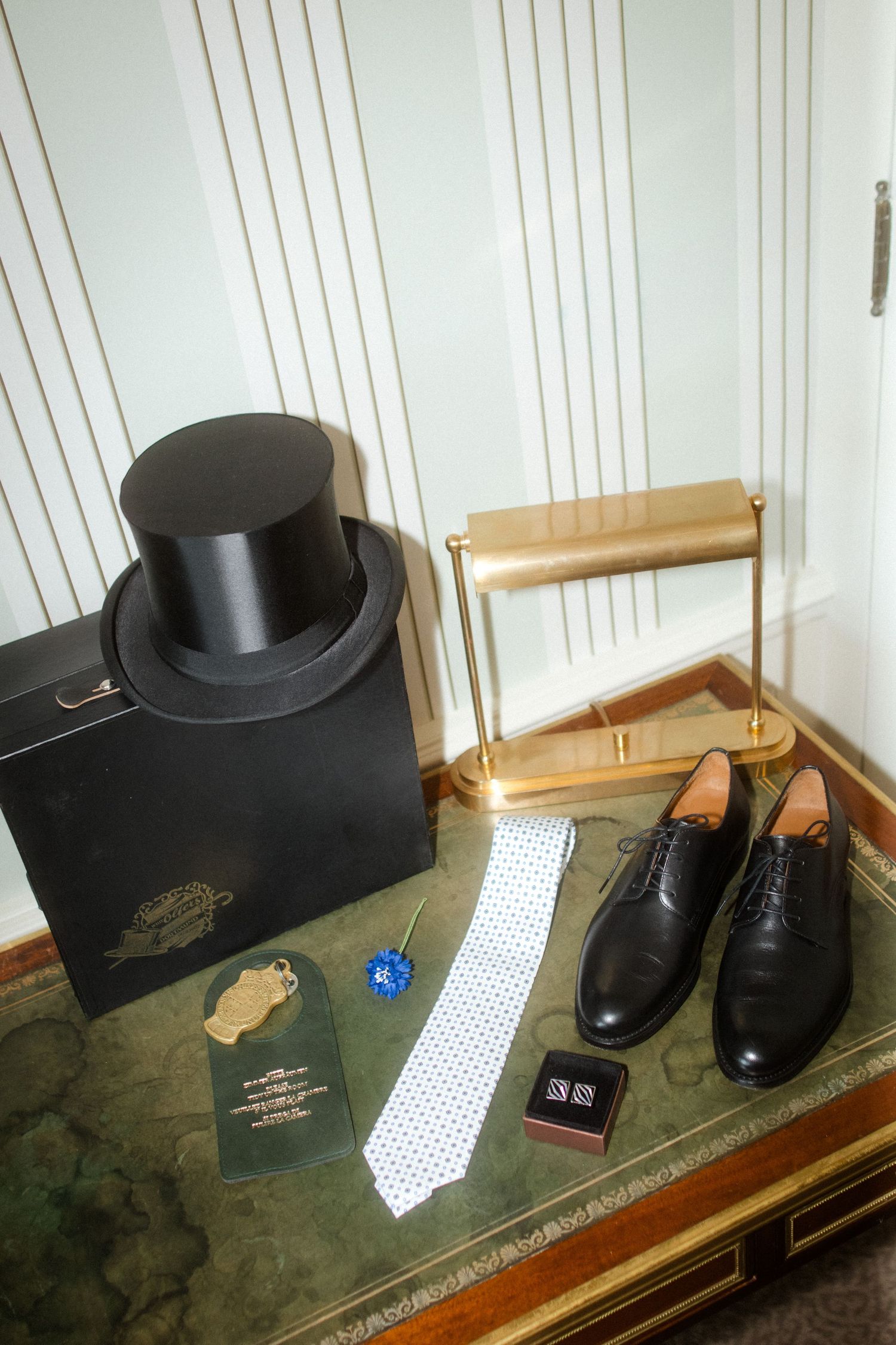 Formal accessories including top hat, tie, and dress shoes arranged on antique table.