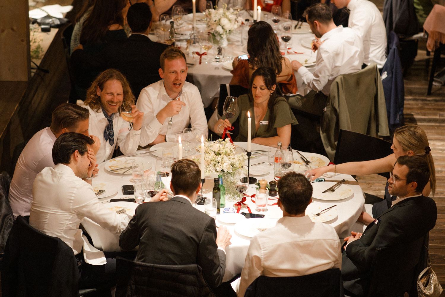 Elegantly dressed guests socializing at round tables during a formal dinner reception.