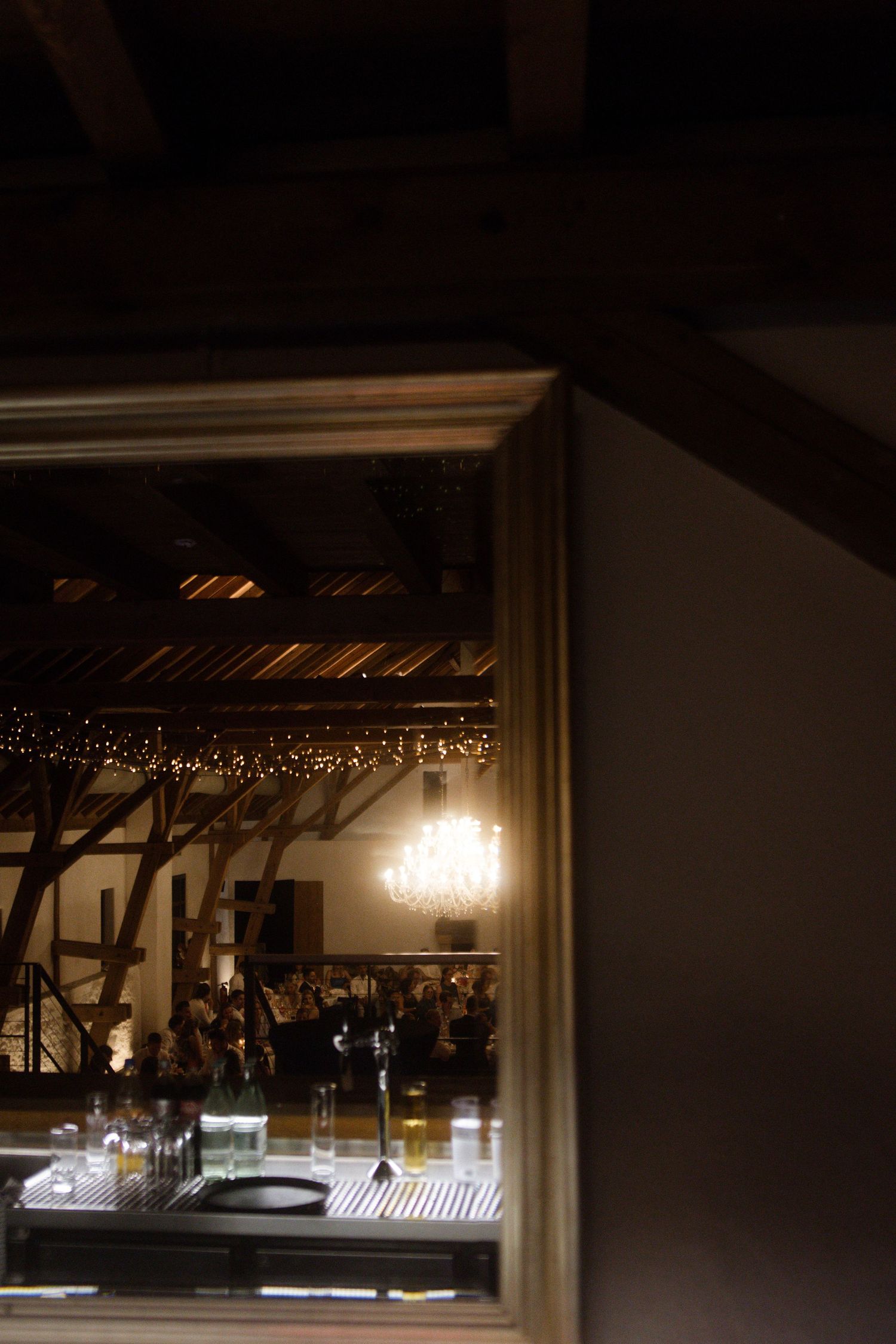 Dimly lit wedding venue seen through doorframe with chandelier glowing in distance.