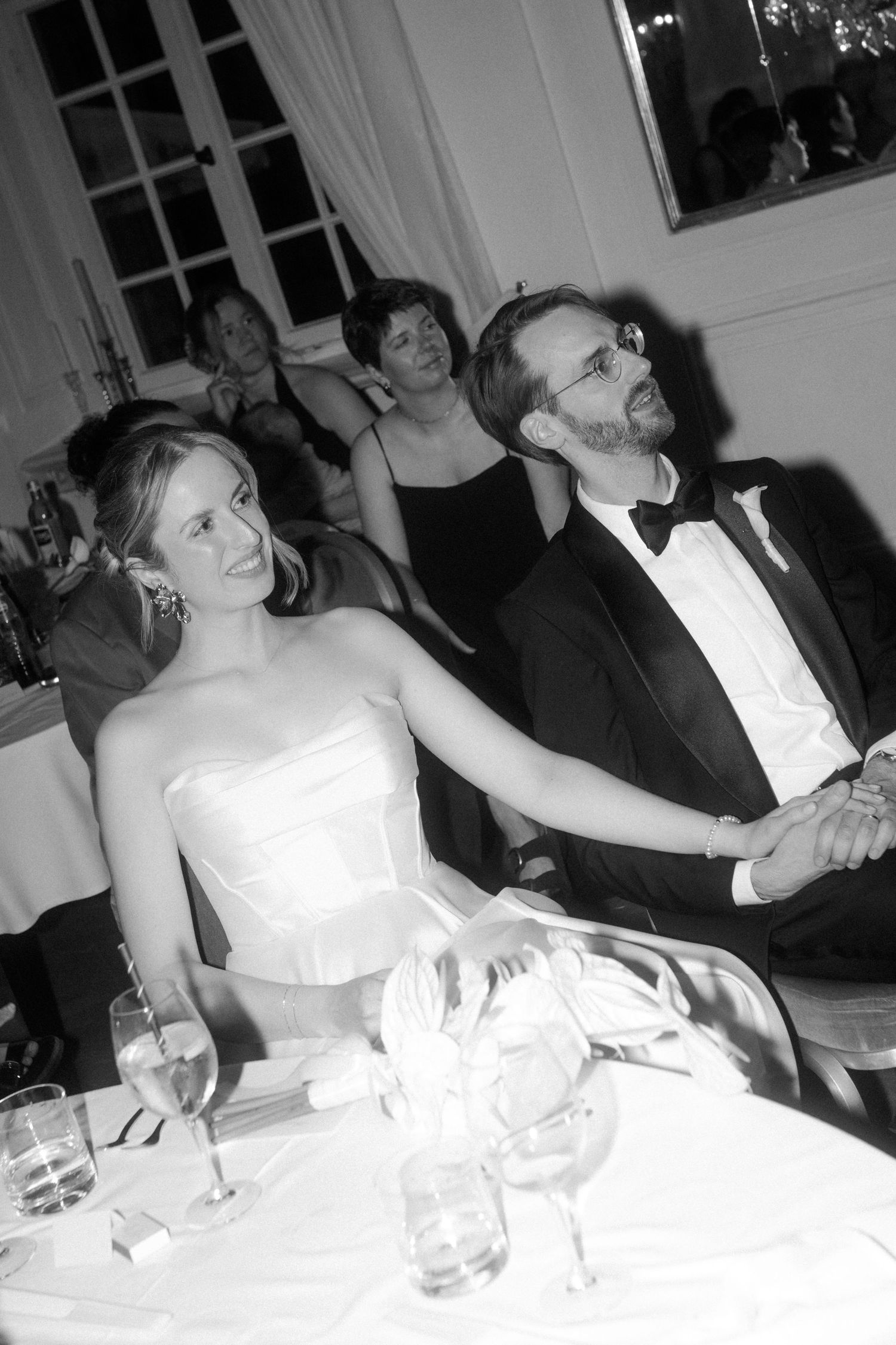 Wedding guests laughing and celebrating at tables during an elegant ballroom reception.