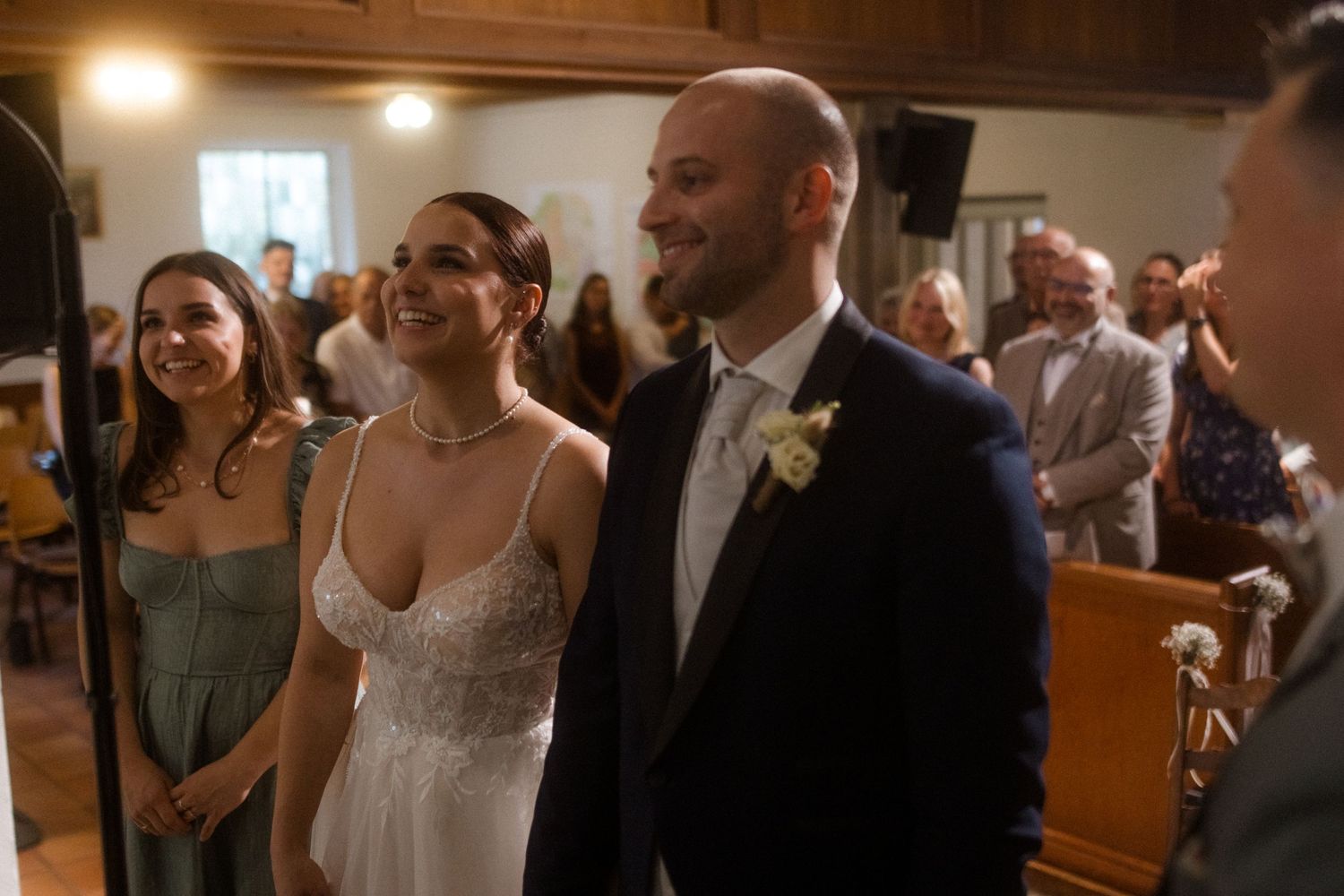 Wedding ceremony attendees smile and laugh together in a church sanctuary.