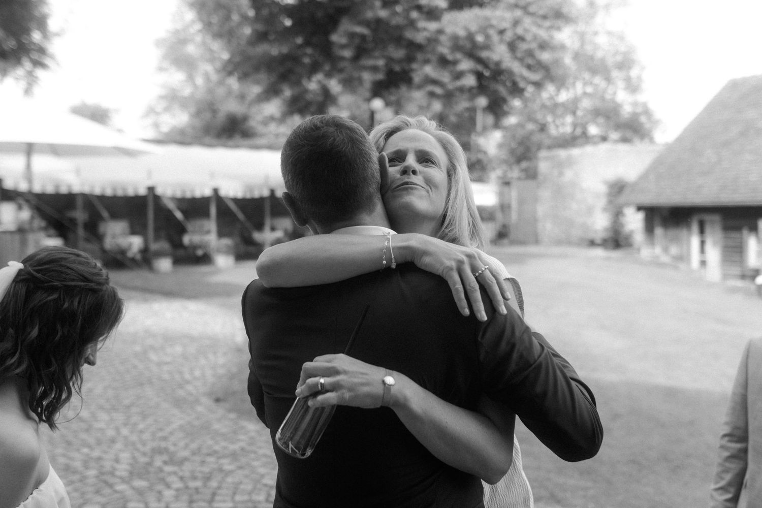 Black and white candid photo of wedding guests embracing during outdoor reception.