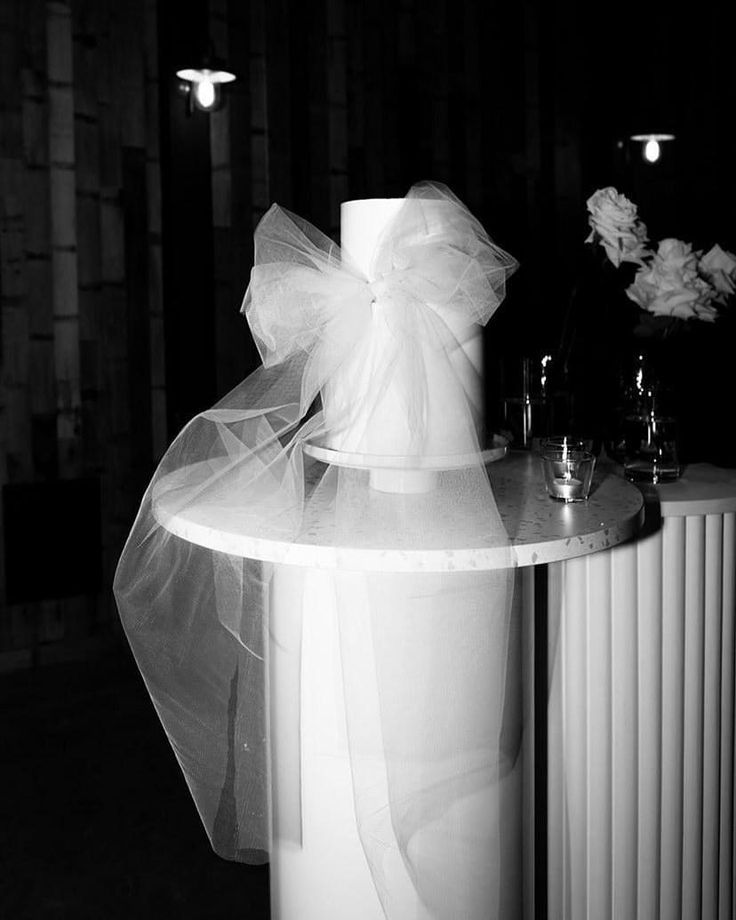 Black and white photo of a tulle bow decoration on a cylindrical pedestal in dim lighting.