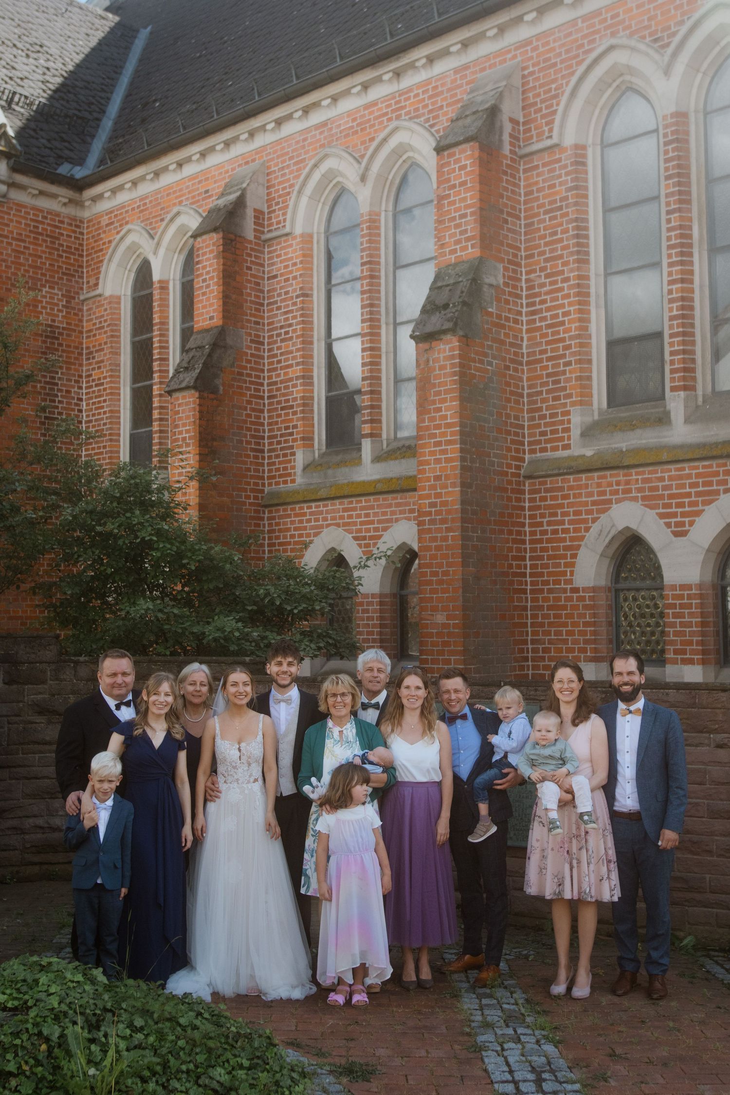 Wedding group photo of family members and wedding party outside historic brick church.