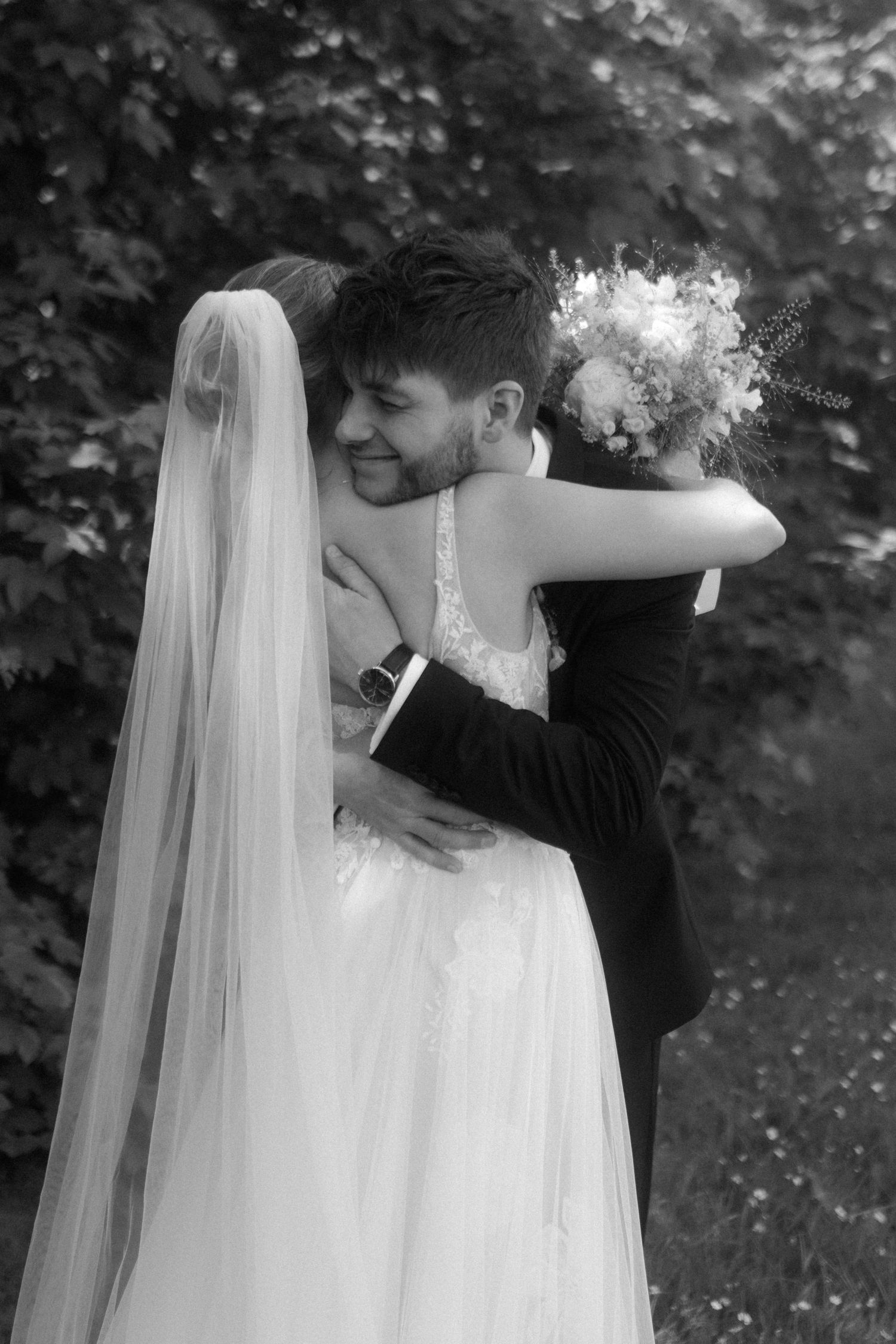 Black and white capture of newlyweds embracing during their wedding in a garden setting.