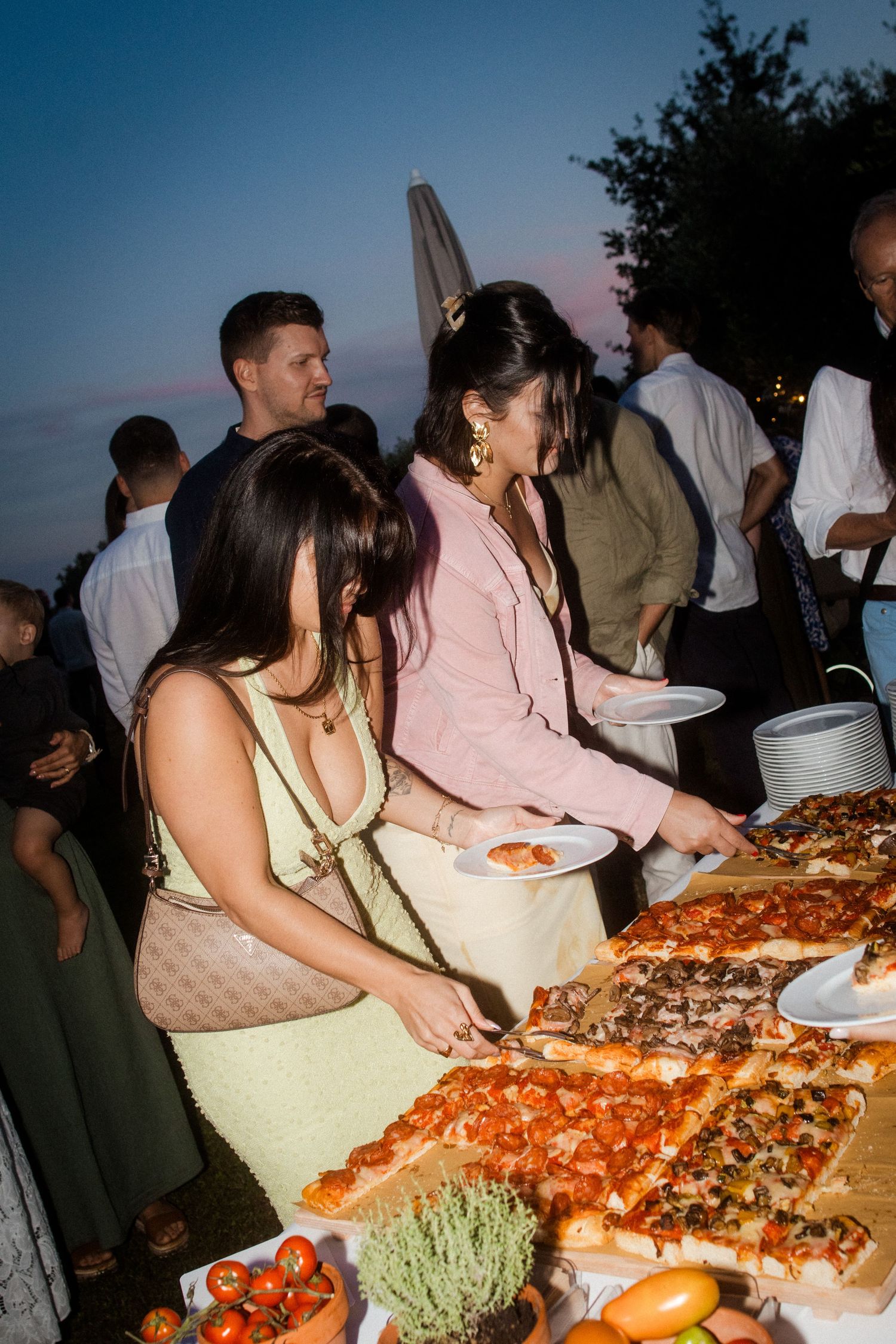 Guests serving themselves from large platters of food at an outdoor evening buffet.