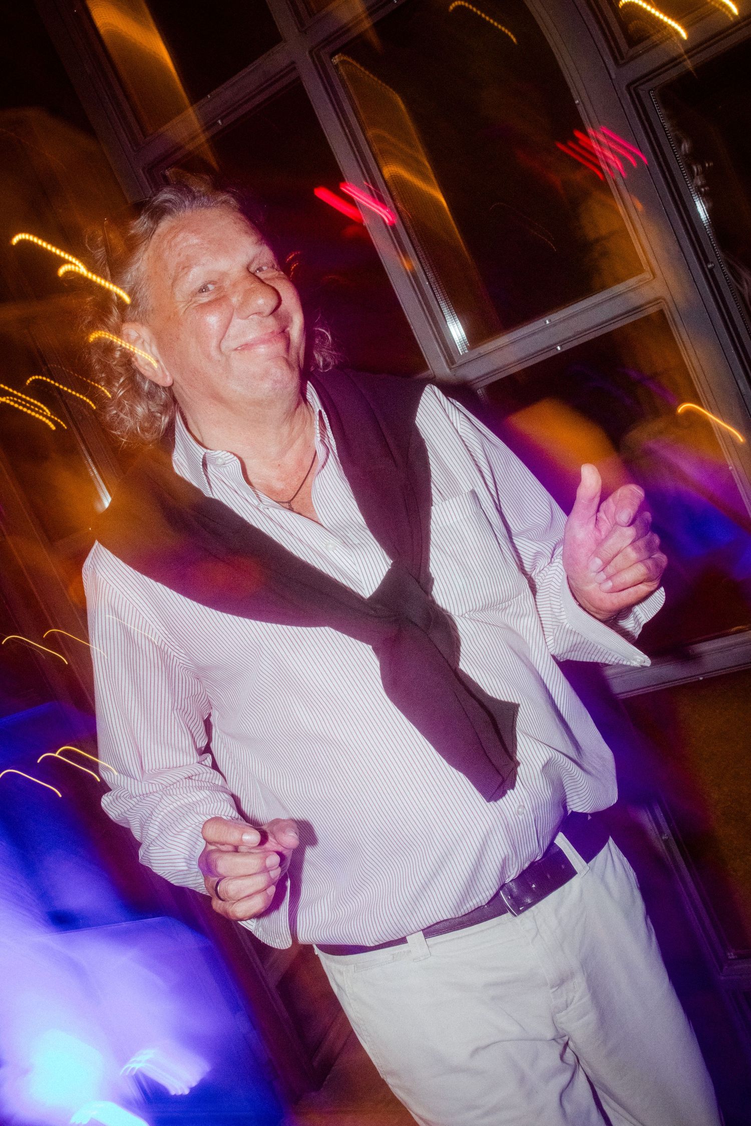 A person in white dances energetically under colorful party lights.