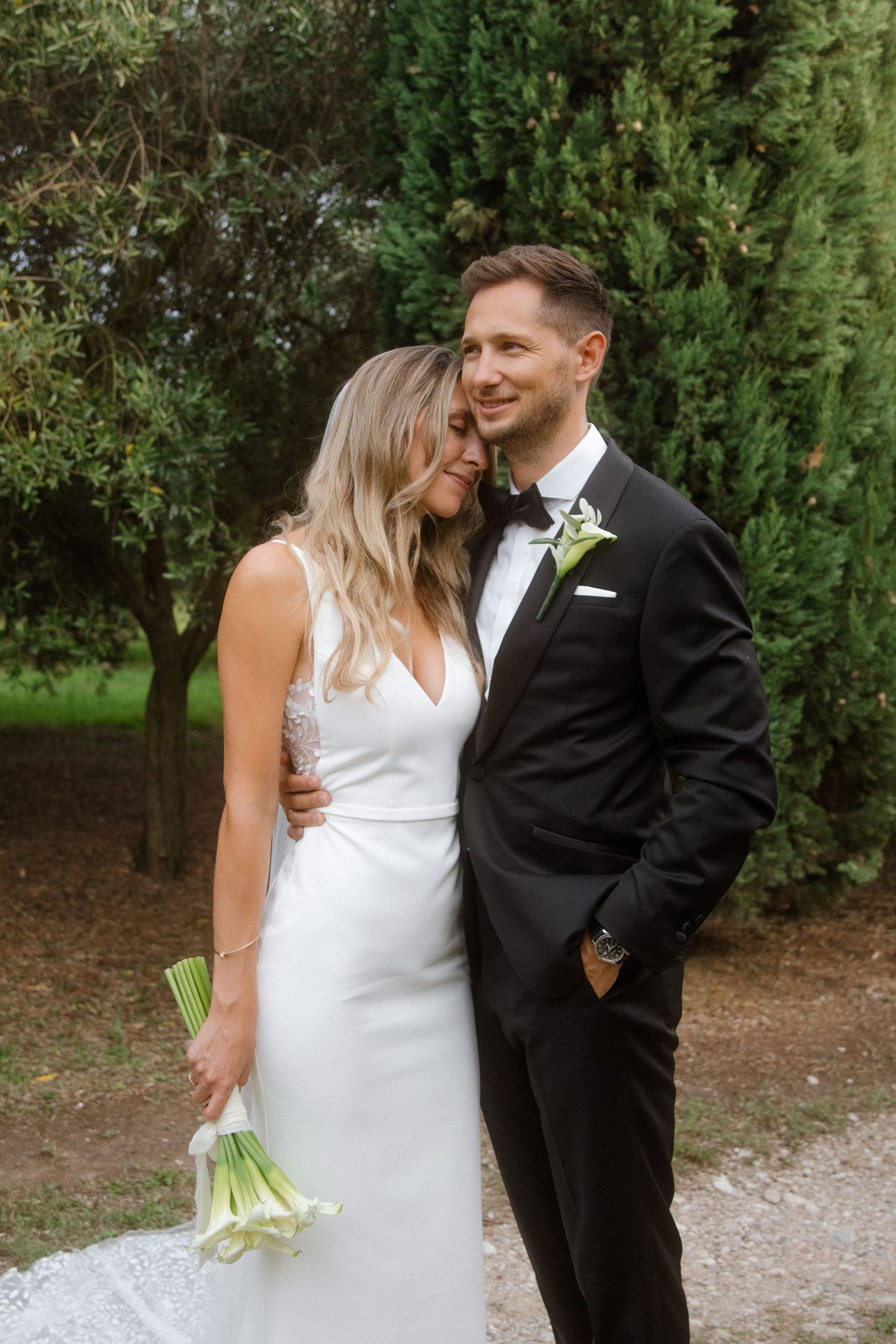 Intimate wedding portrait of a couple in formal attire standing among garden greenery.