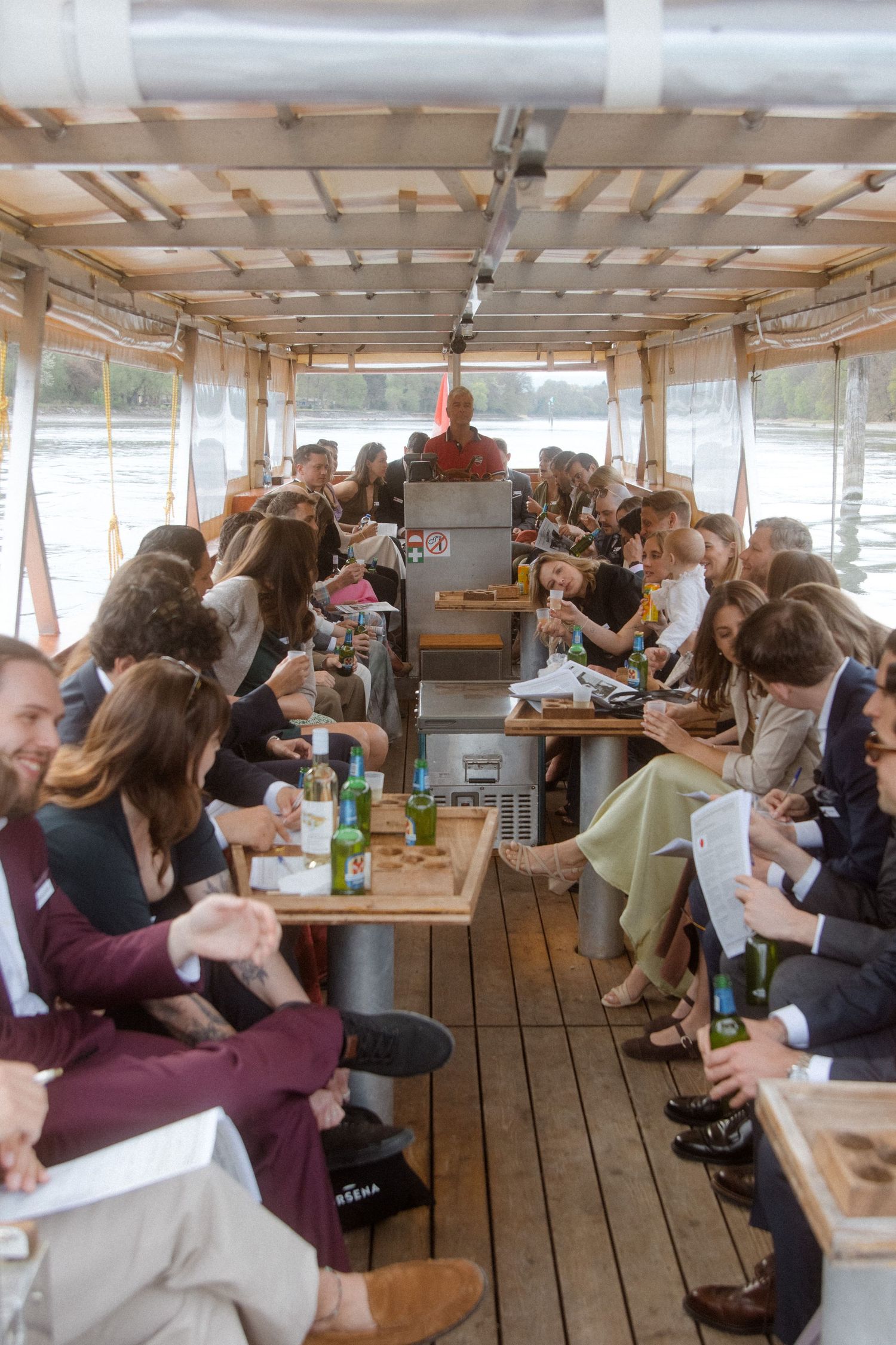 Wedding guests seated inside a wooden river boat enjoying drinks and conversation during a cruise.