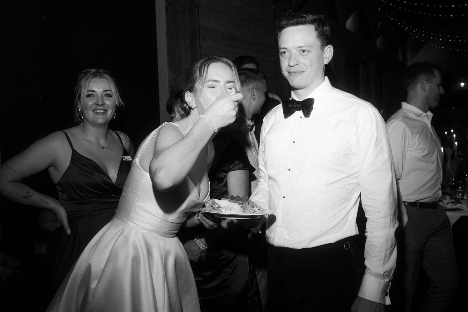 Bride eating wedding cake while groom holds the plate at a black and white reception.