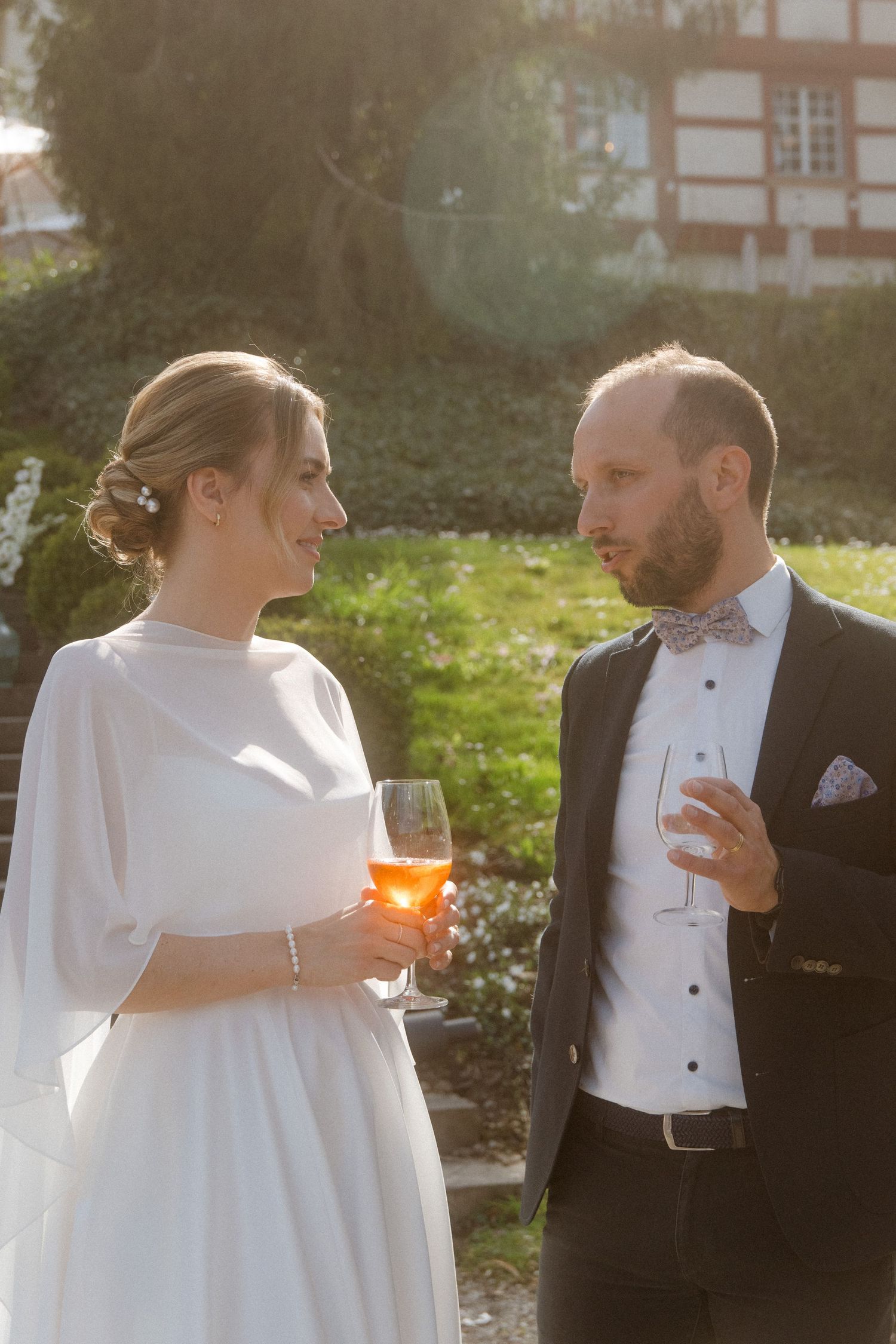 Bride and groom toasting with wine glasses outdoors in golden sunlight at their wedding reception.