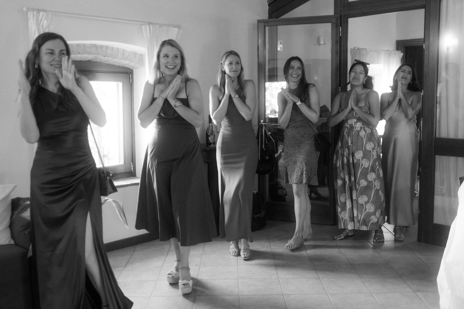 People in colorful dresses gather in a bright indoor hallway for photos.