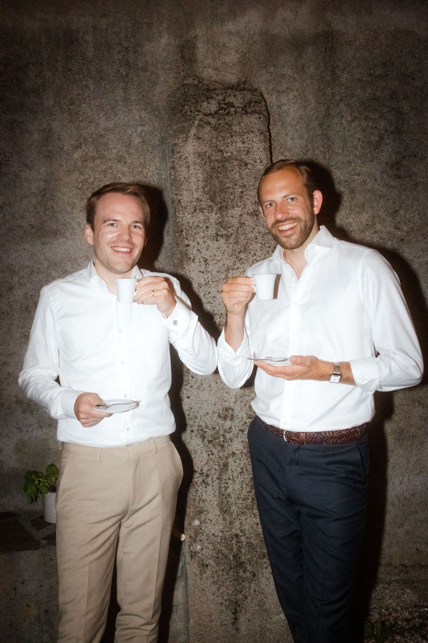 Wedding guests posing playfully against textured wall at evening celebration.