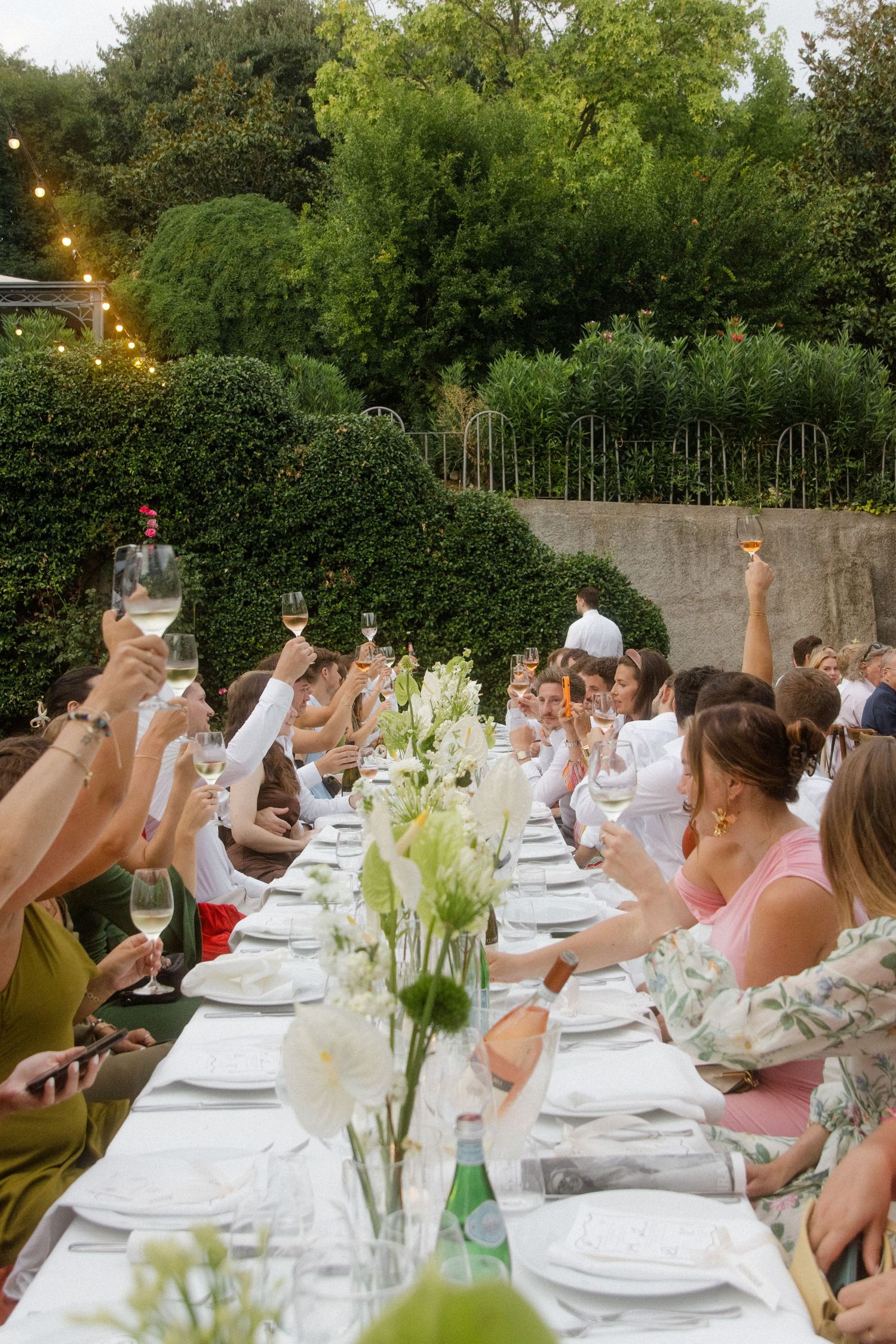 Guests seated at long white tables for an outdoor wedding dinner with floral centerpieces.