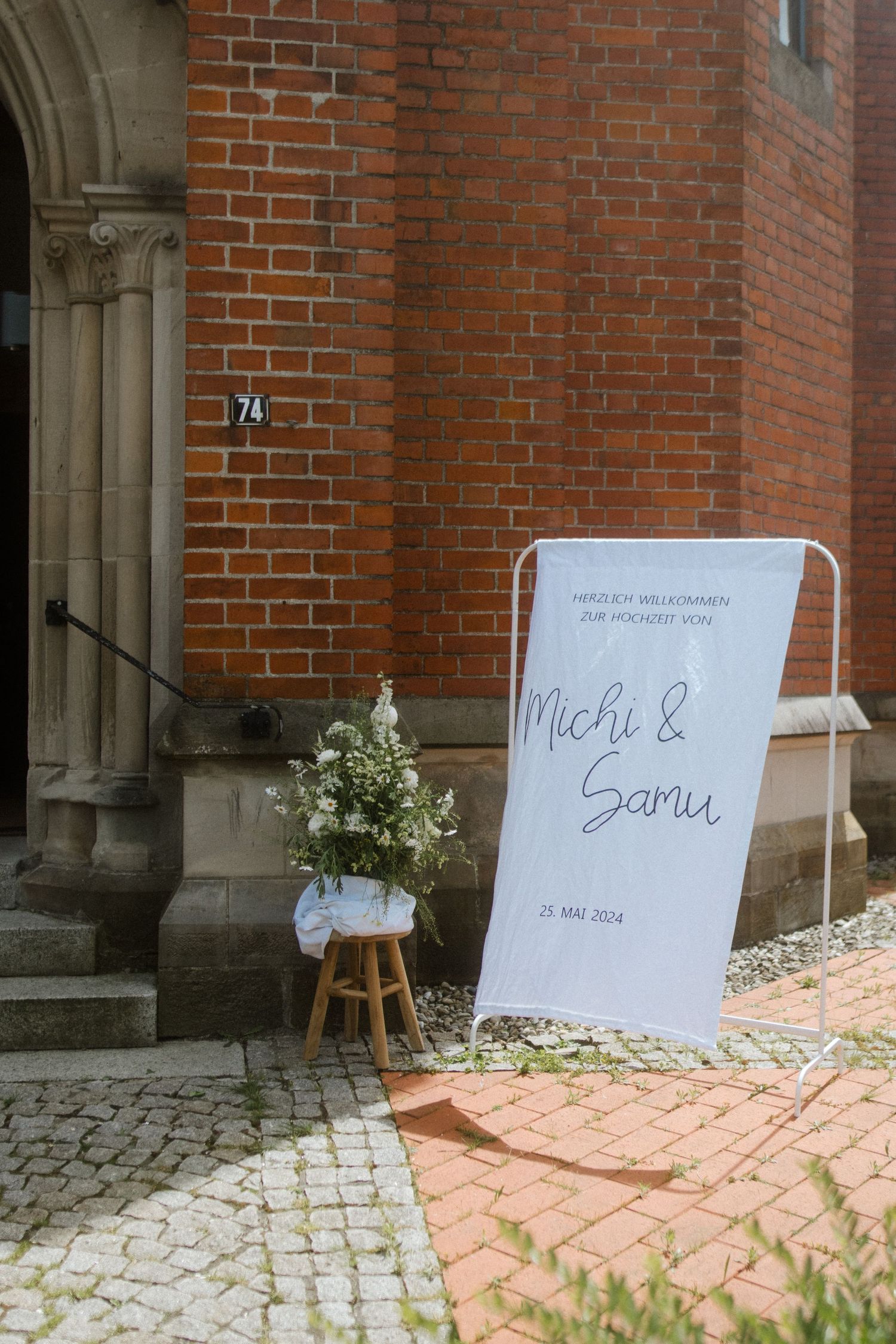 Wedding welcome sign and floral arrangement outside brick church entrance.