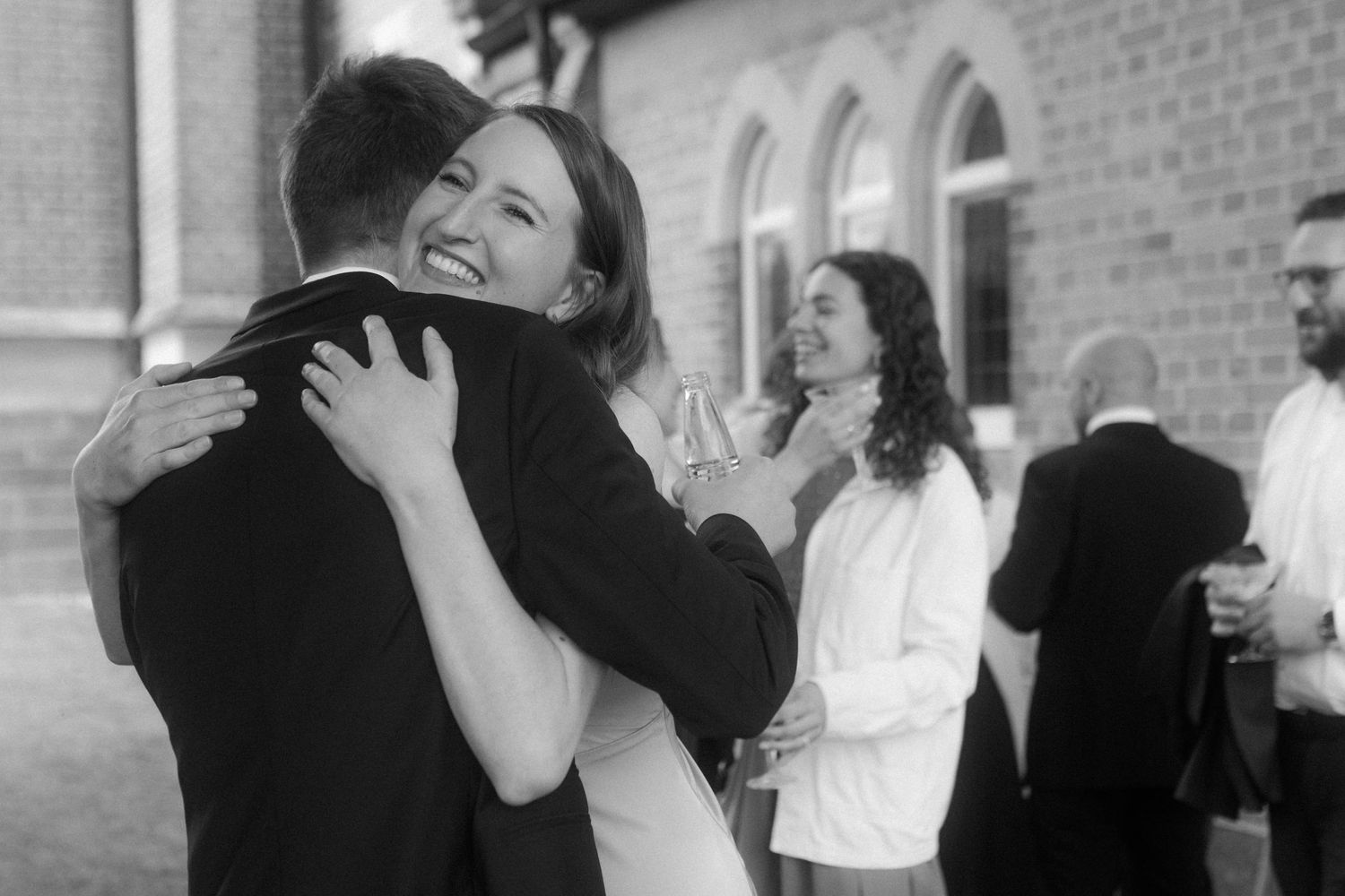 Black and white photo capturing emotional hug during outdoor wedding celebration.
