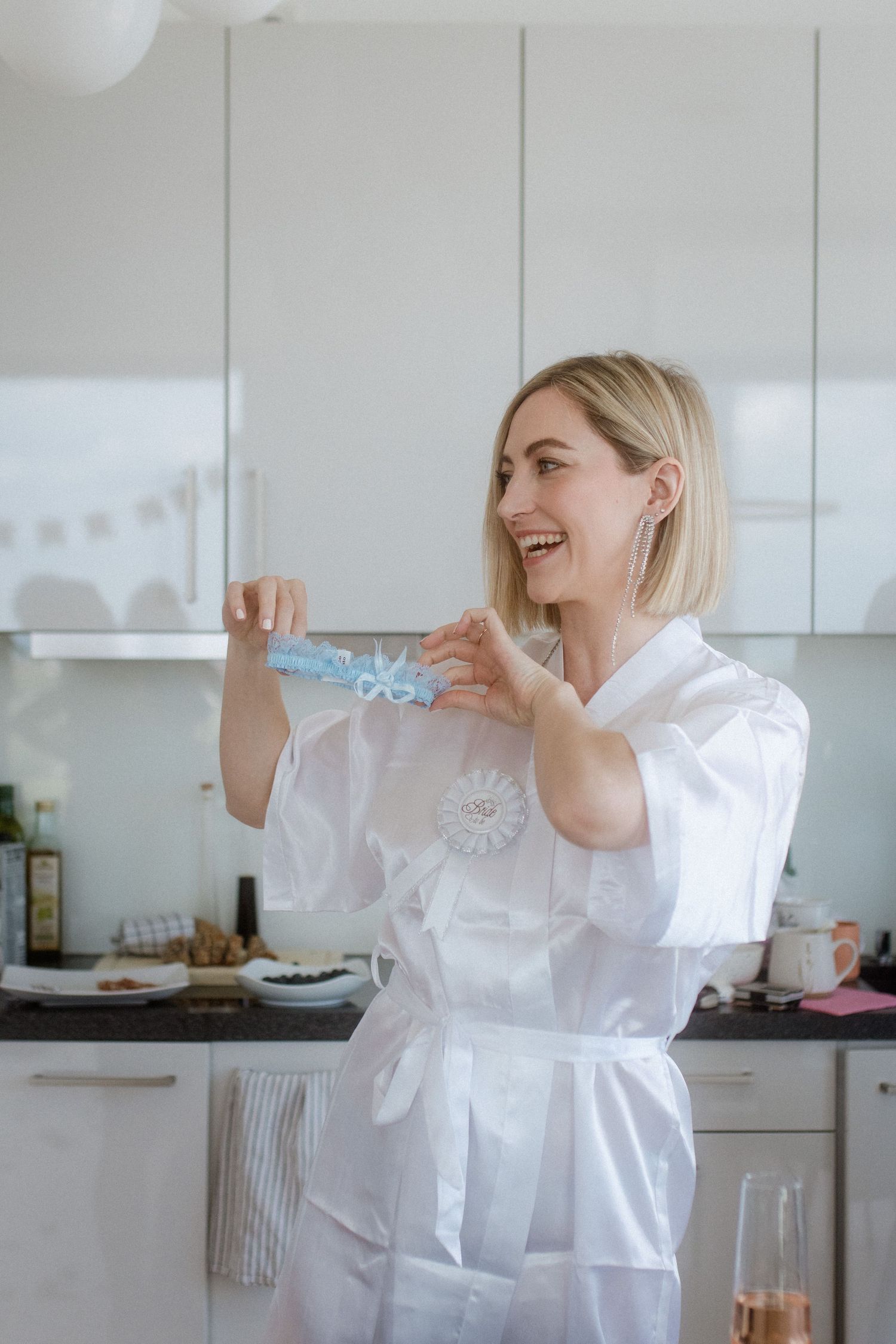 Person in white robe holding up small blue accessory in modern kitchen.
