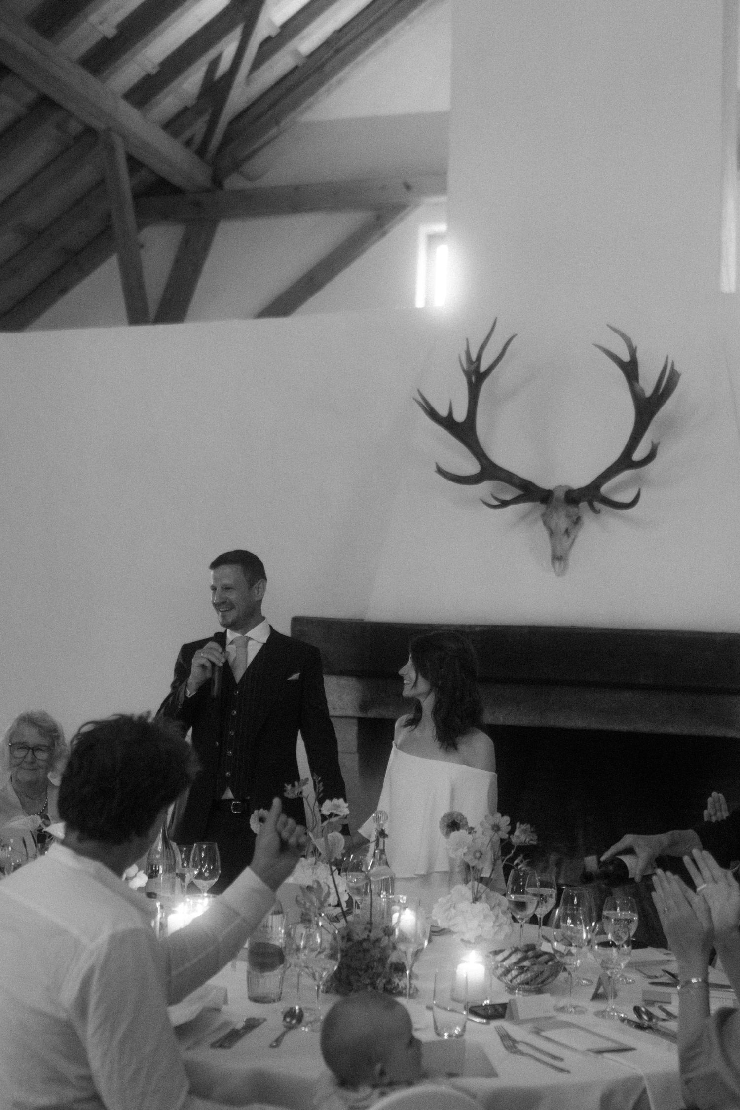 Wedding reception speech in rustic venue with antler decor and candlelit table settings.