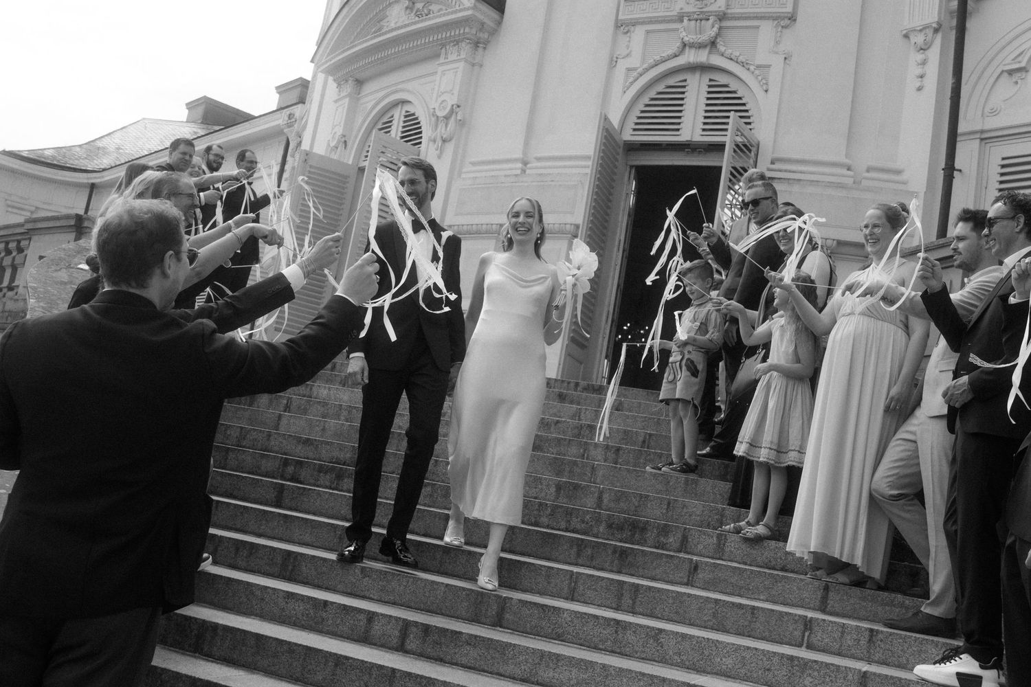 Guests celebrate on the steps of a classical building during a wedding ceremony exit.