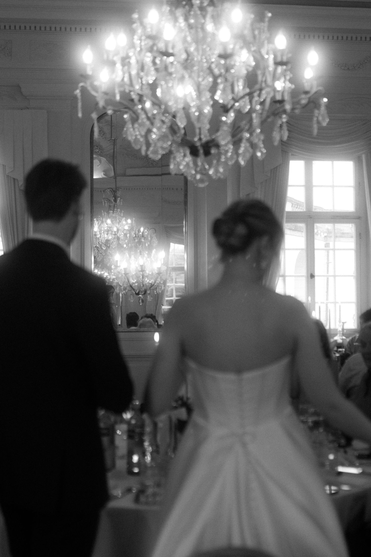 Wedding celebration under sparkling crystal chandeliers in an elegant white room.