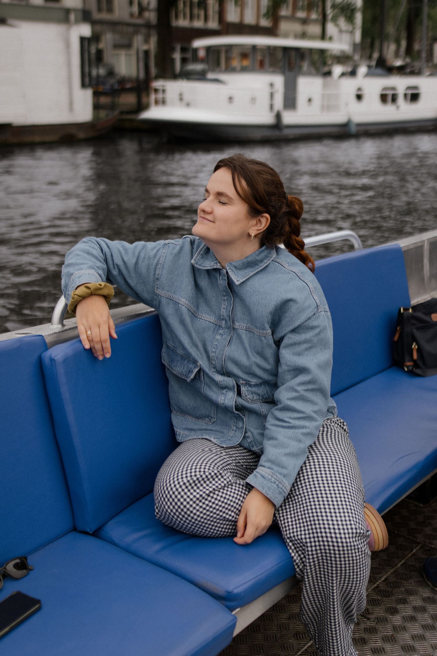 Person lounging on blue cushioned seating along a canal in Amsterdam wearing checkered pants.