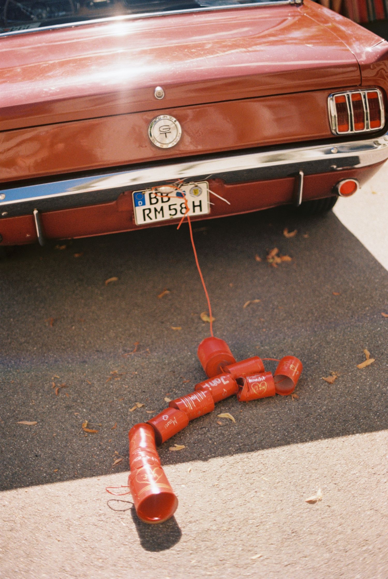 Red tin cans tied to a vintage car bumper trail behind on the pavement.