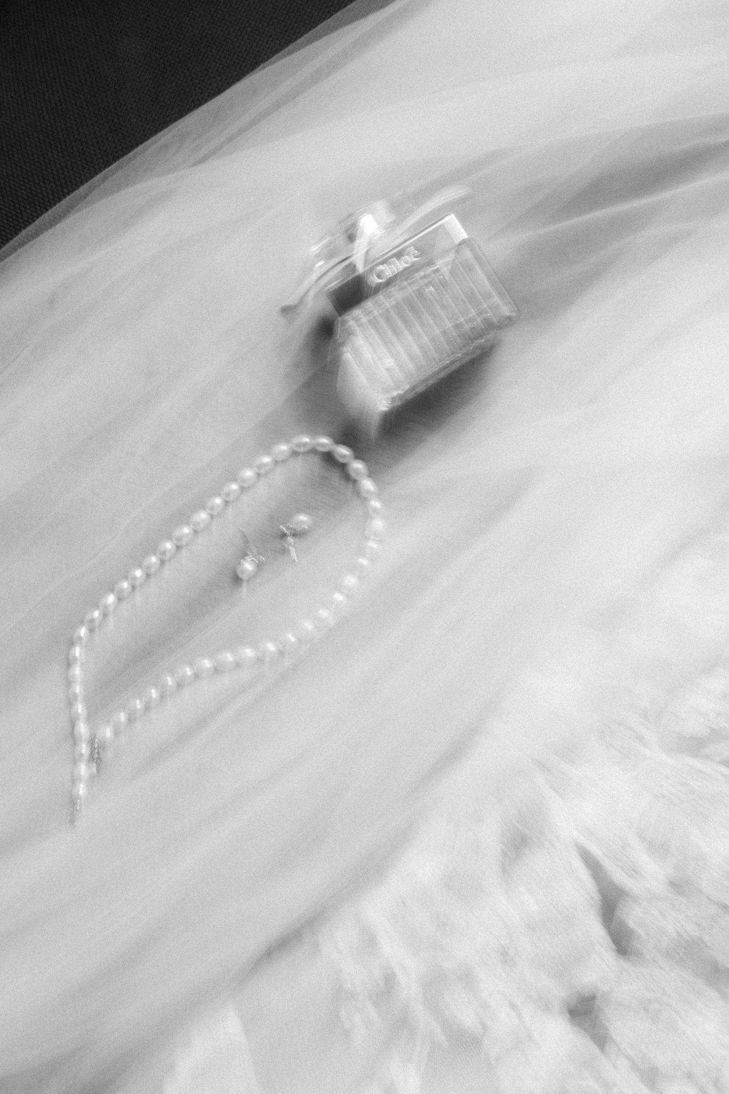 Dreamy black and white photo of wedding accessories with perfume bottle and pearls on tulle.