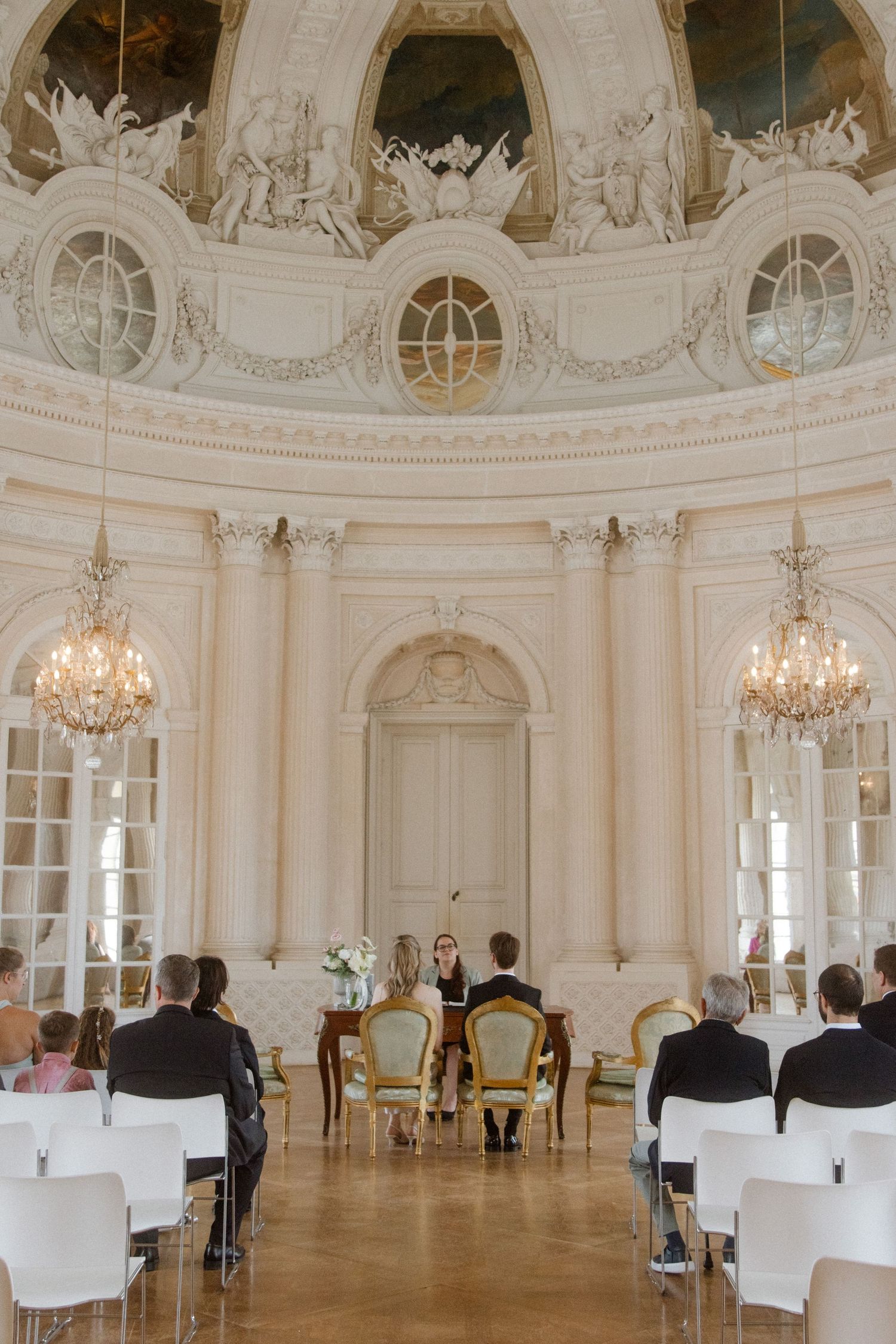 A grand baroque wedding venue with ornate ceiling frescoes and crystal chandeliers.
