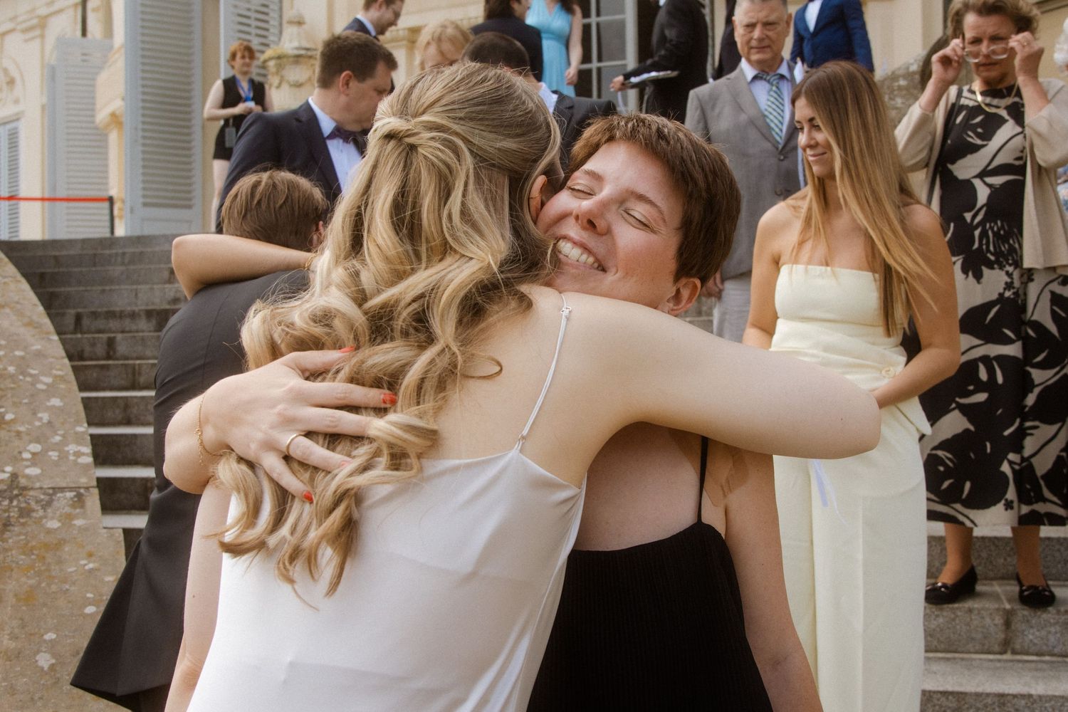 Wedding guests share warm embraces during the celebration outside a historic venue.