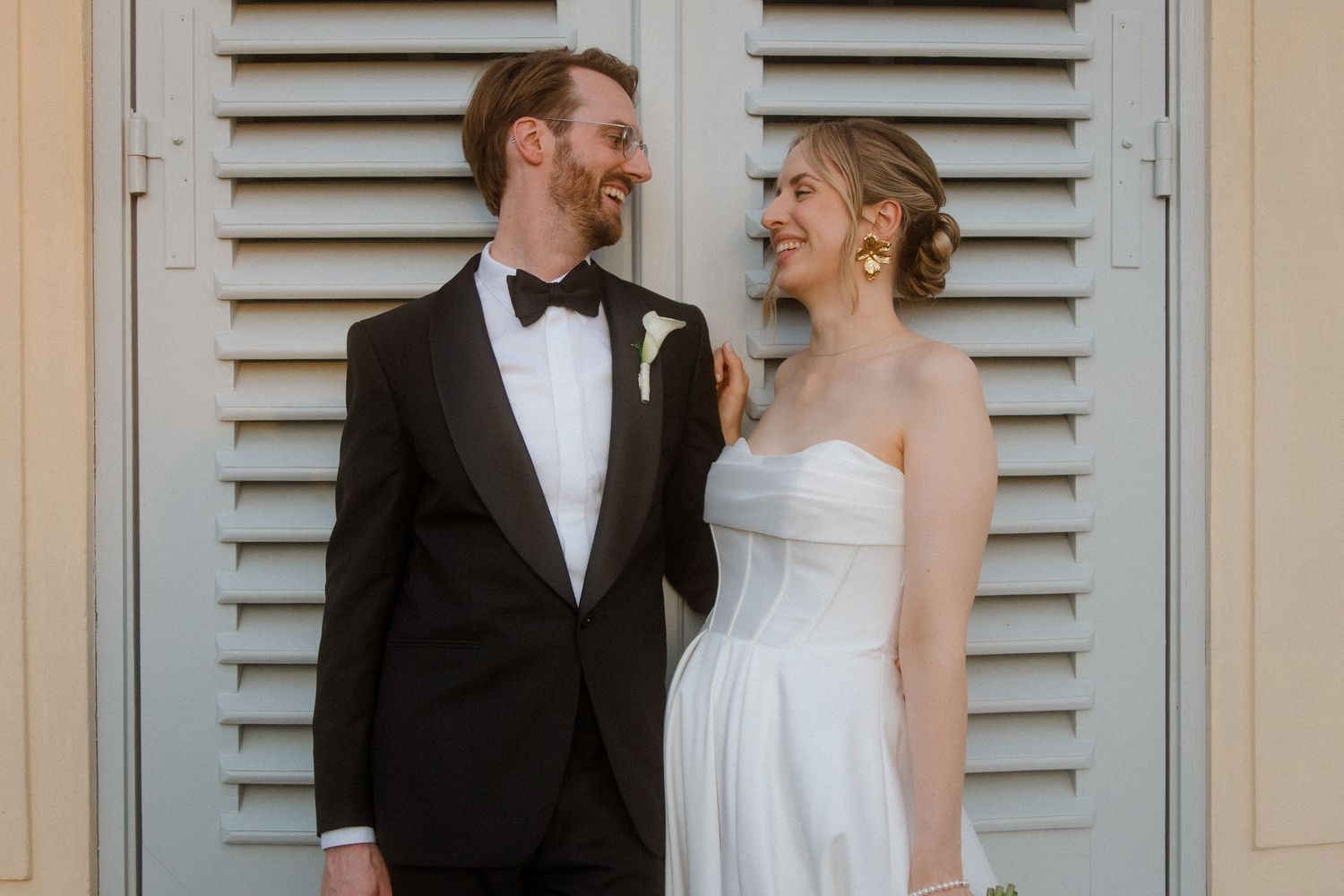 Elegant wedding couple posing against a wall with classic shuttered windows.