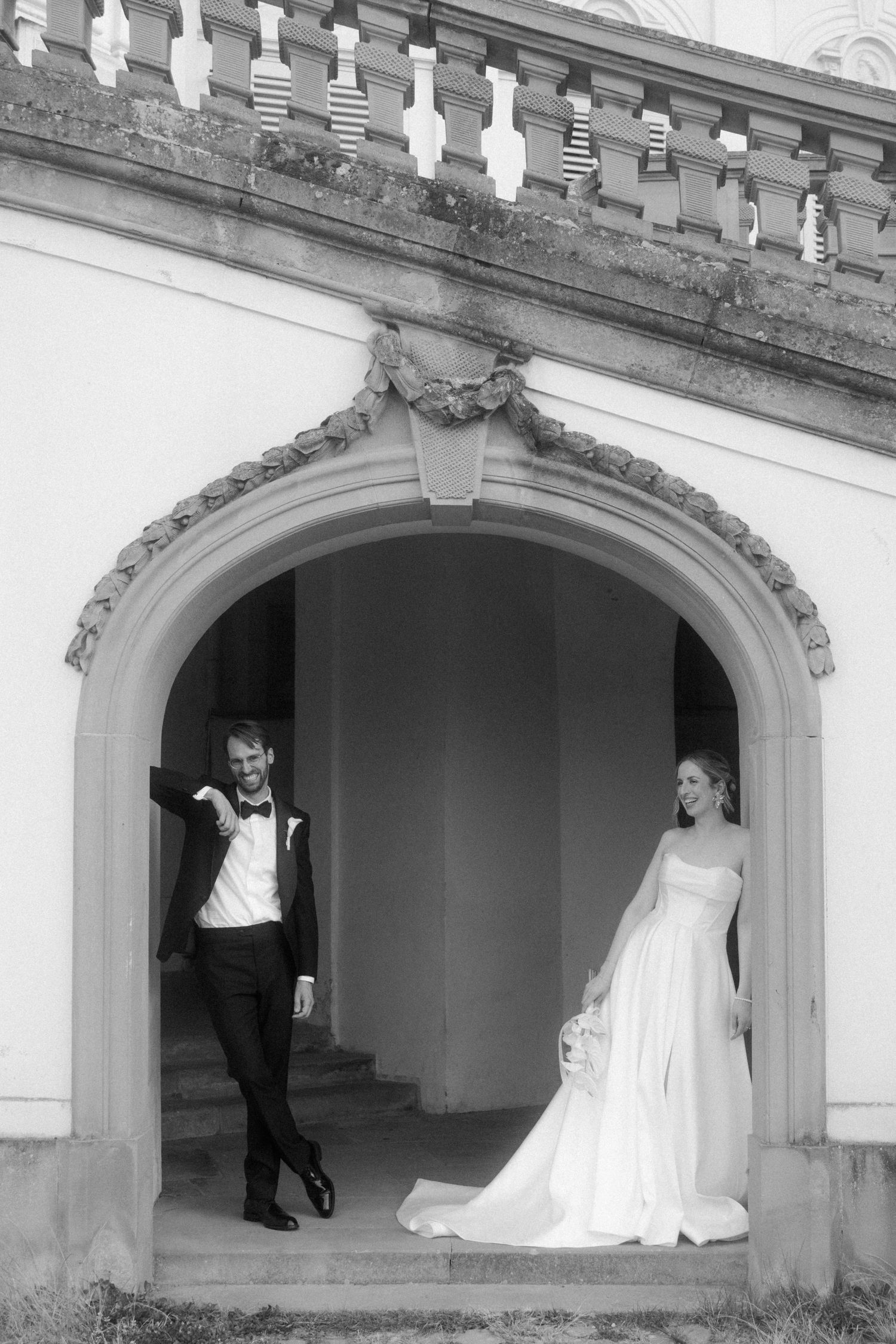 Black and white photo of figures in formal attire posing in arched architectural spaces.