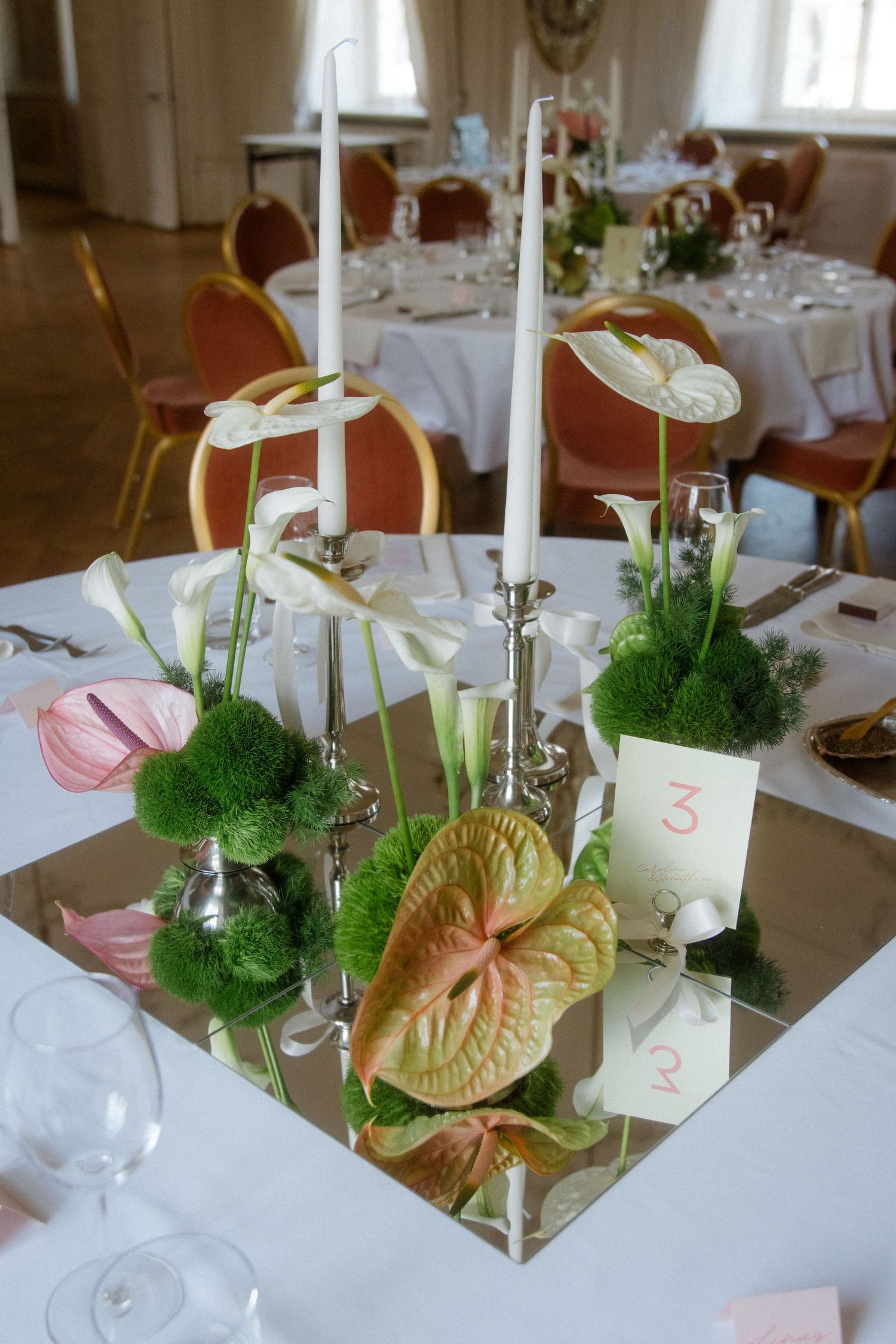 Wedding table centerpiece with green moss balls, anthurium flowers and white candles.