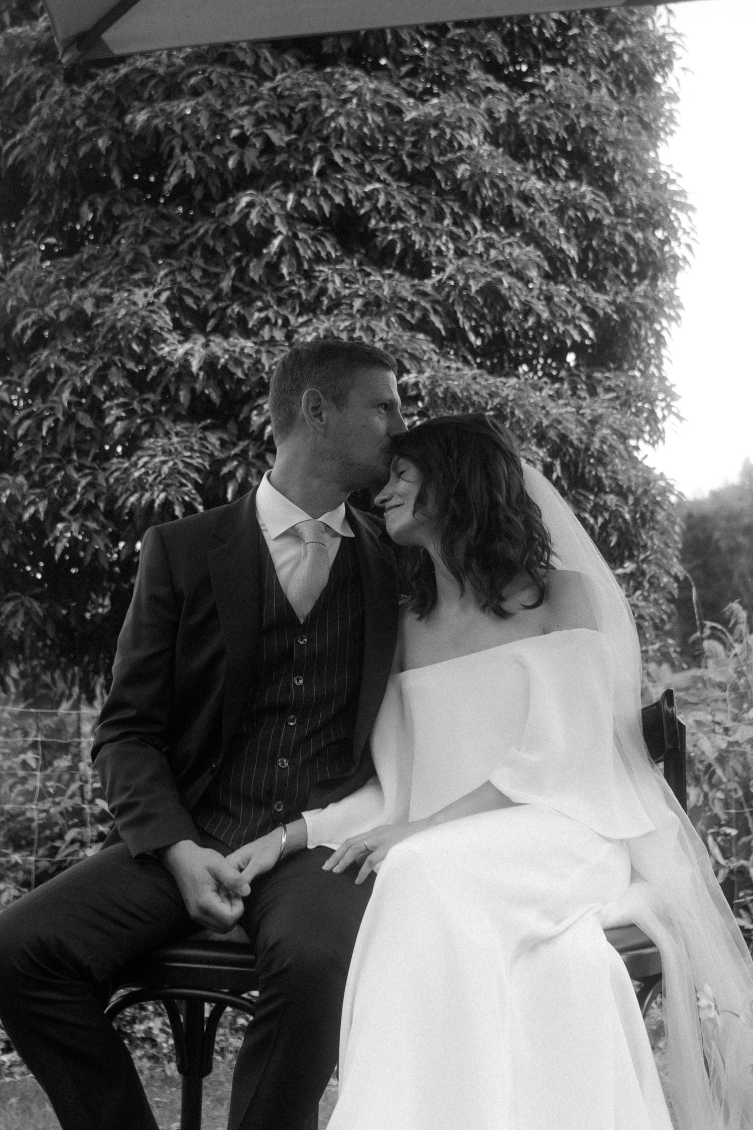 Tender moment between newlyweds sitting together in garden setting.