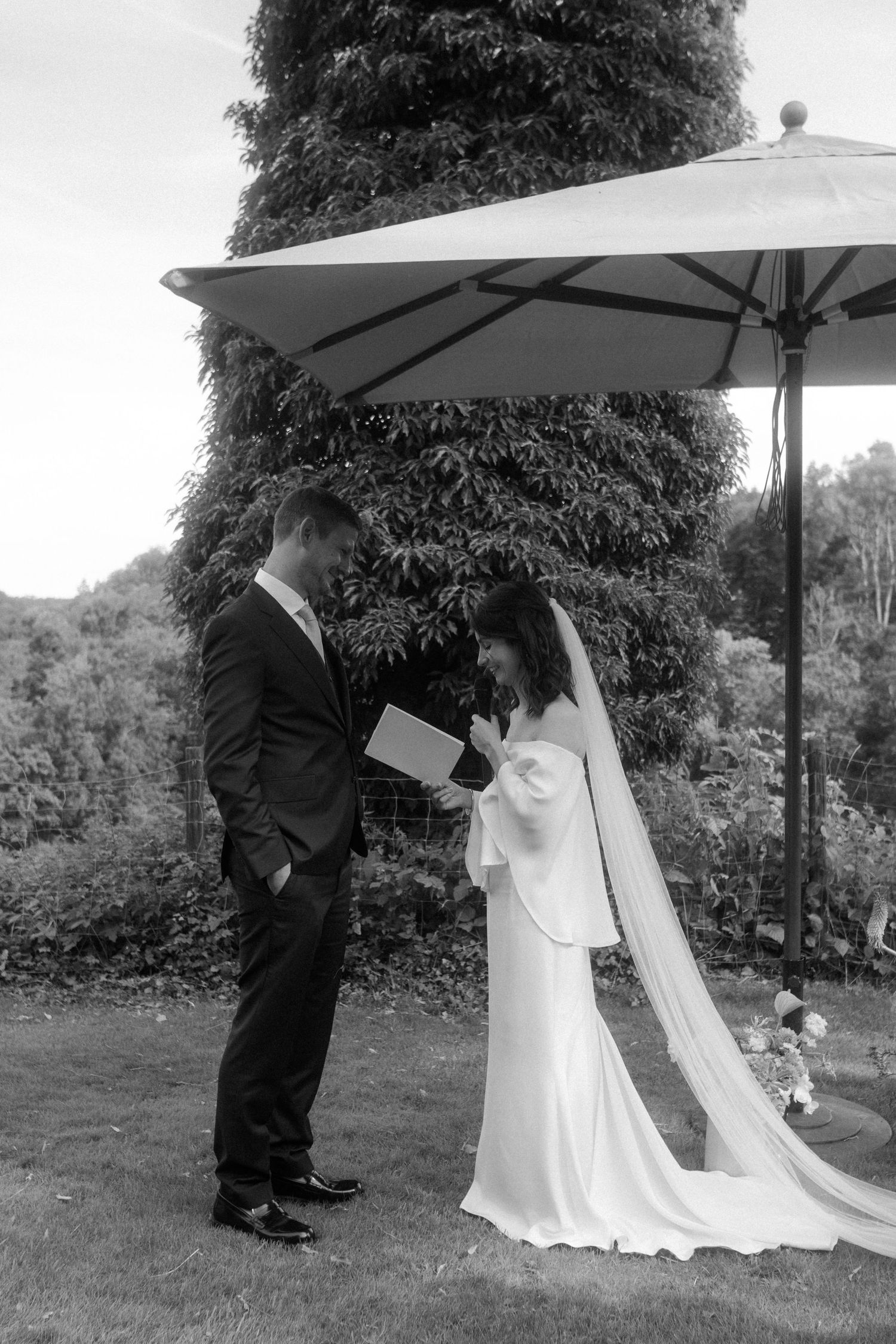Black and white photo of a couple during their outdoor wedding ceremony under a white umbrella.