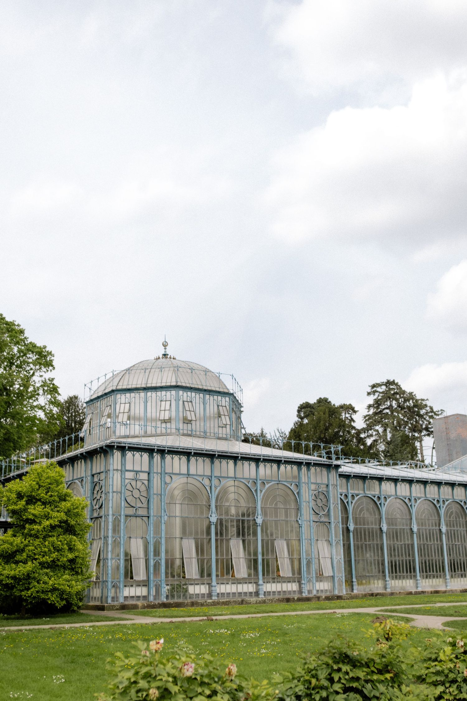 Historic glass conservatory building with domed roof and ornate architecture in a garden setting.