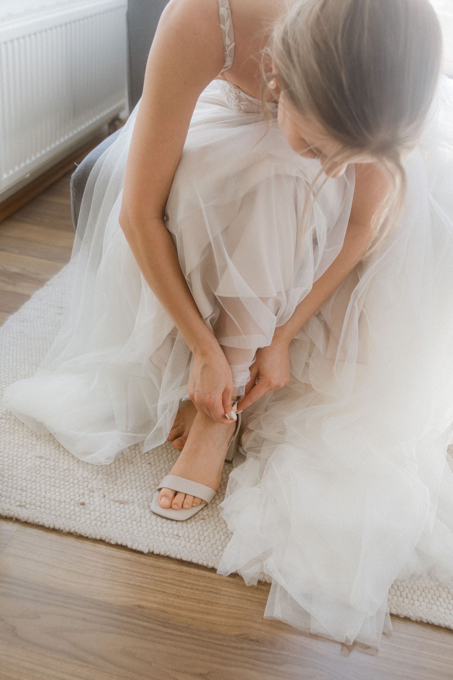 Close-up of delicate wedding sandals being fastened on feet draped in white tulle.