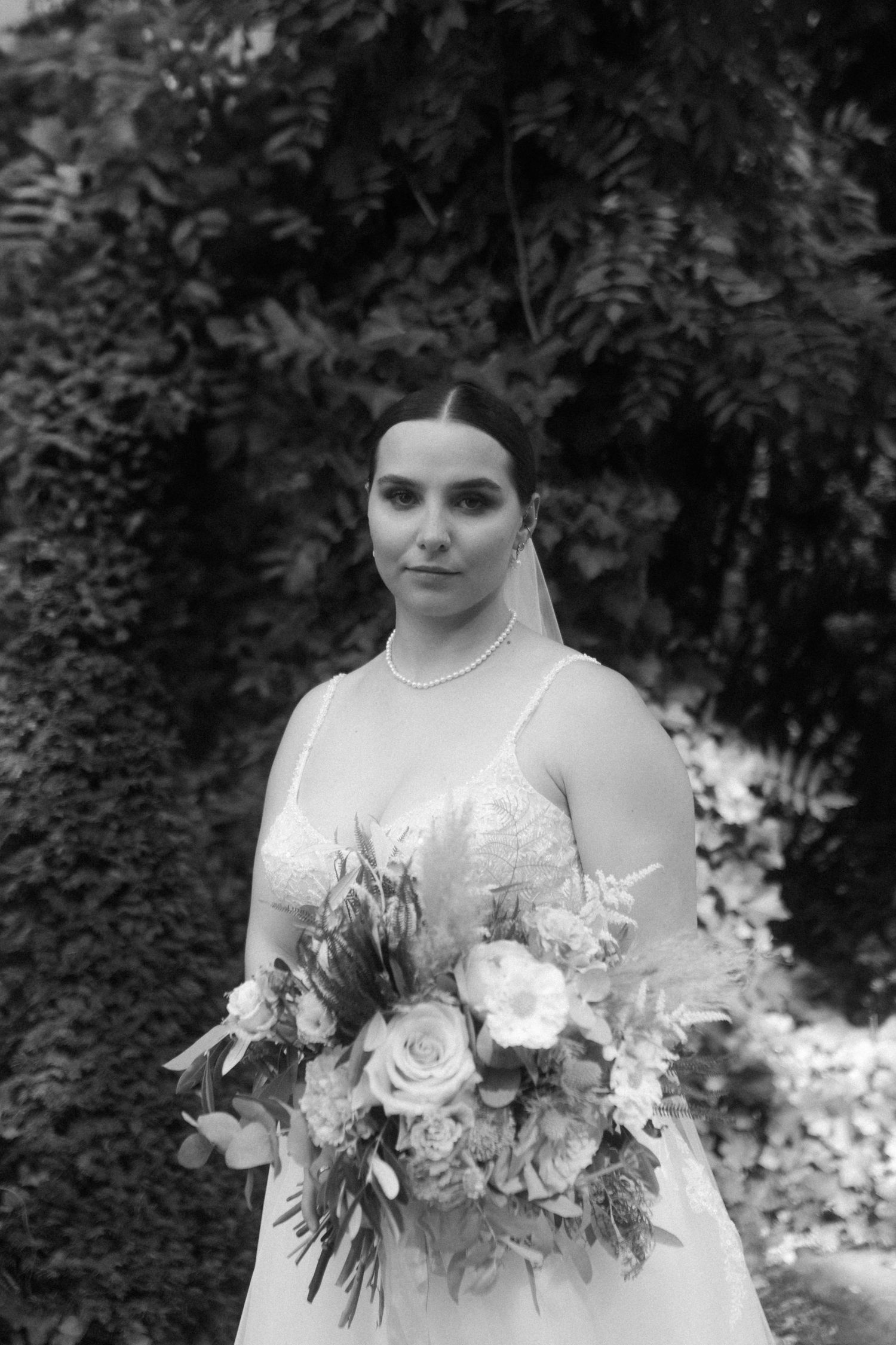 Elegant bridal portrait in black and white featuring a classic wedding dress and statement floral bouquet.