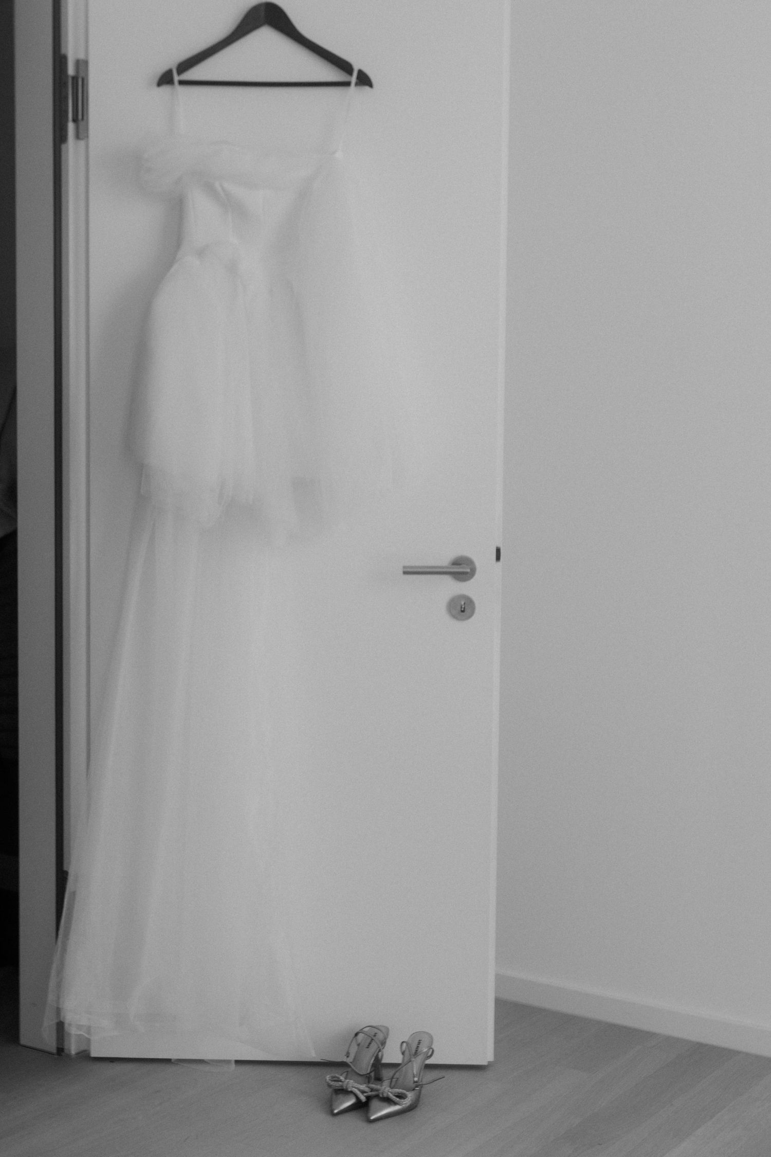 Minimalist black and white photo of wedding dress hanging with shoes beneath.