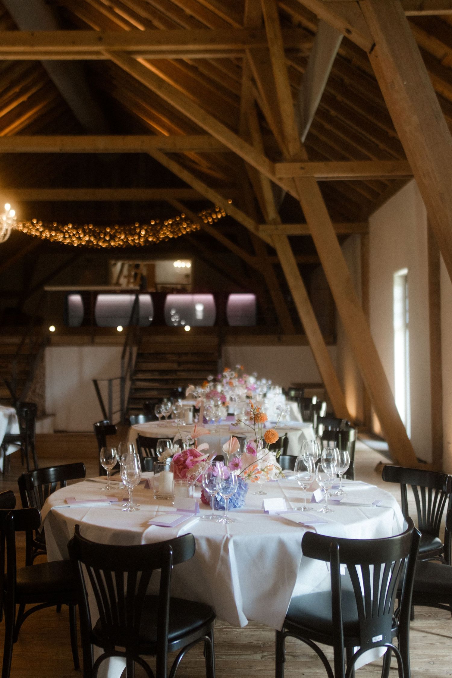 Rustic barn wedding reception venue with exposed wooden beams and twinkling string lights overhead.