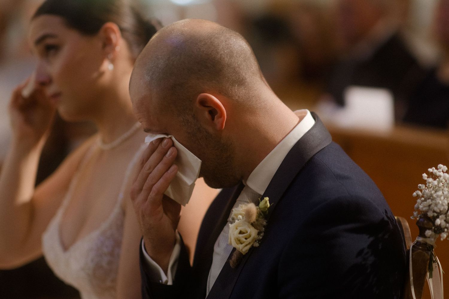 An emotional moment captured during a wedding ceremony as a groom wipes away tears in a navy suit.