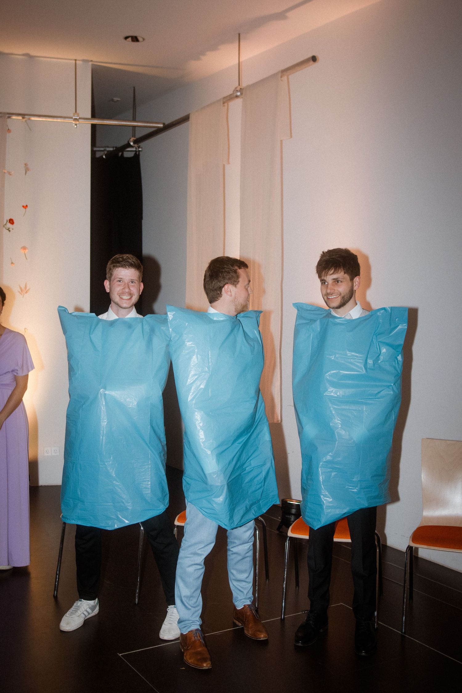 Three people wearing bright blue plastic bag costumes pose together at a party.