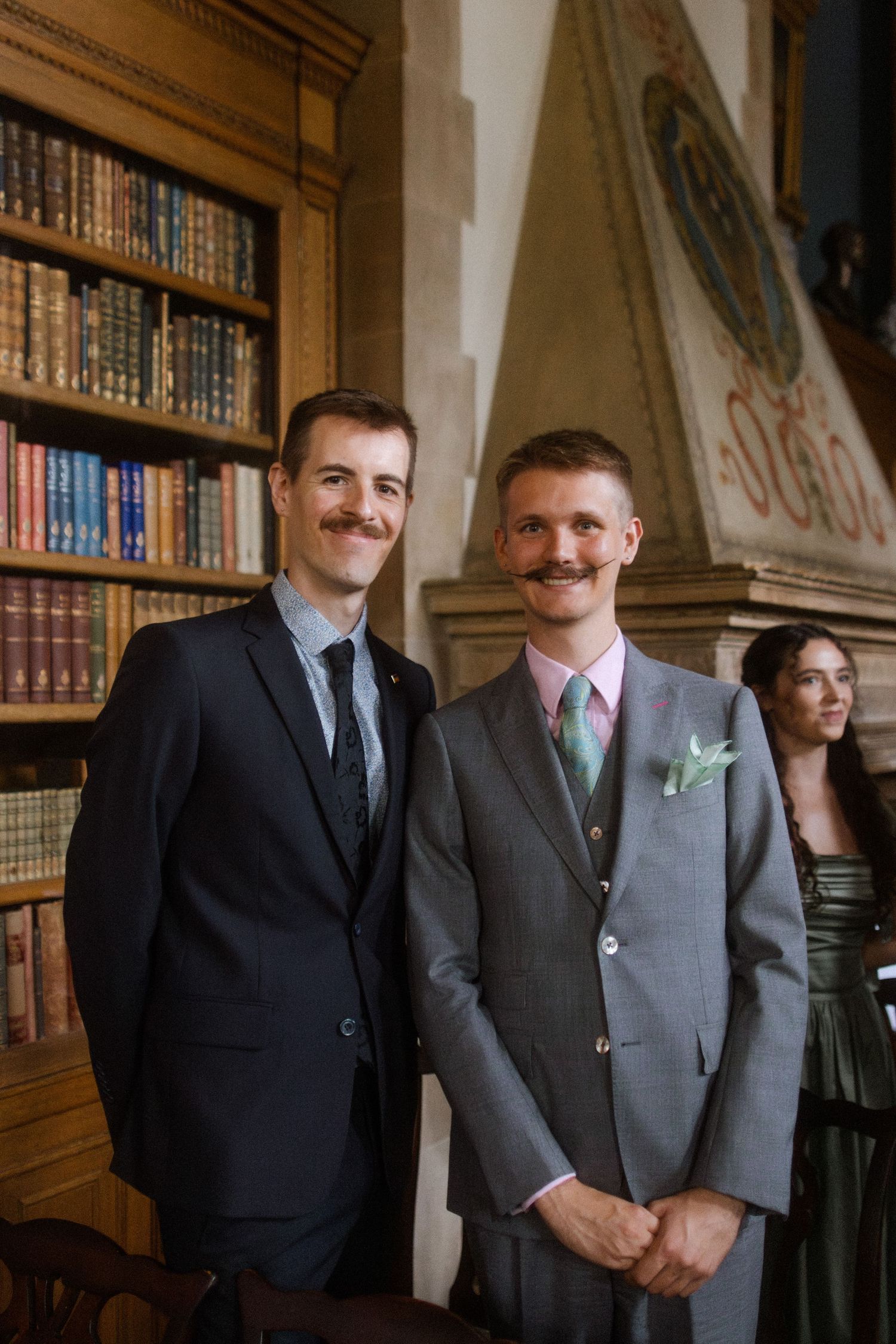 Groomsmen in formal attire posing in library with wooden bookshelves.